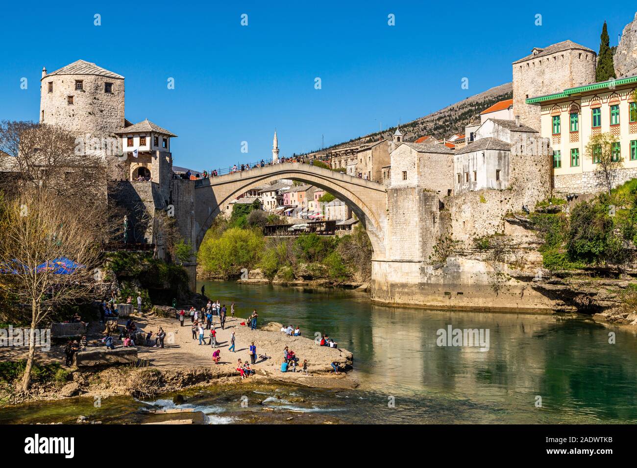 Persone giocare e rilassarsi lungo la riva del fiume Neretva, passeggiata sul ricostruito Stari vecchio ponte di questa storica area balcanica,Mostar, Bosnia Erzegovina Foto Stock