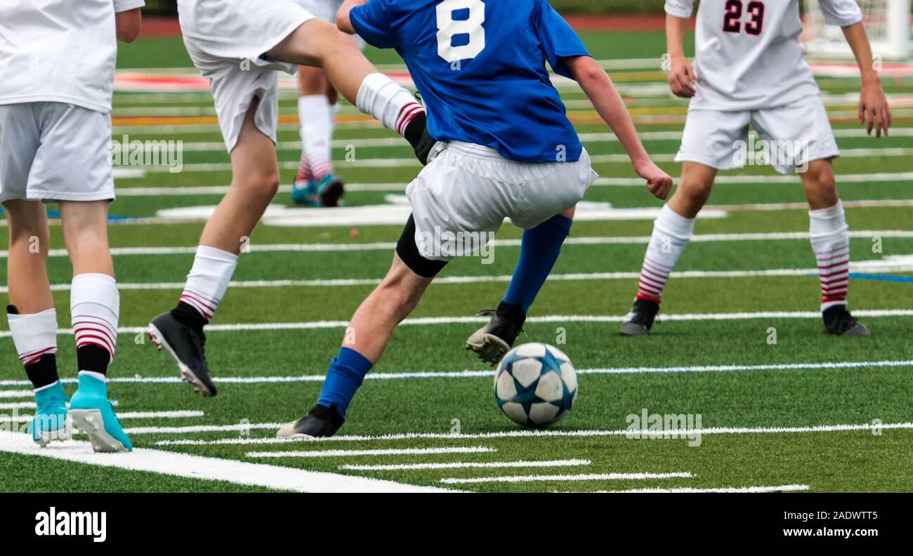 Una scuola di giocatore di calcio è fuori numerate dalla sua concorrenza facendo una mossa per cercare di arrivare intorno a loro durante una partita su un campo di tappeto erboso. Foto Stock