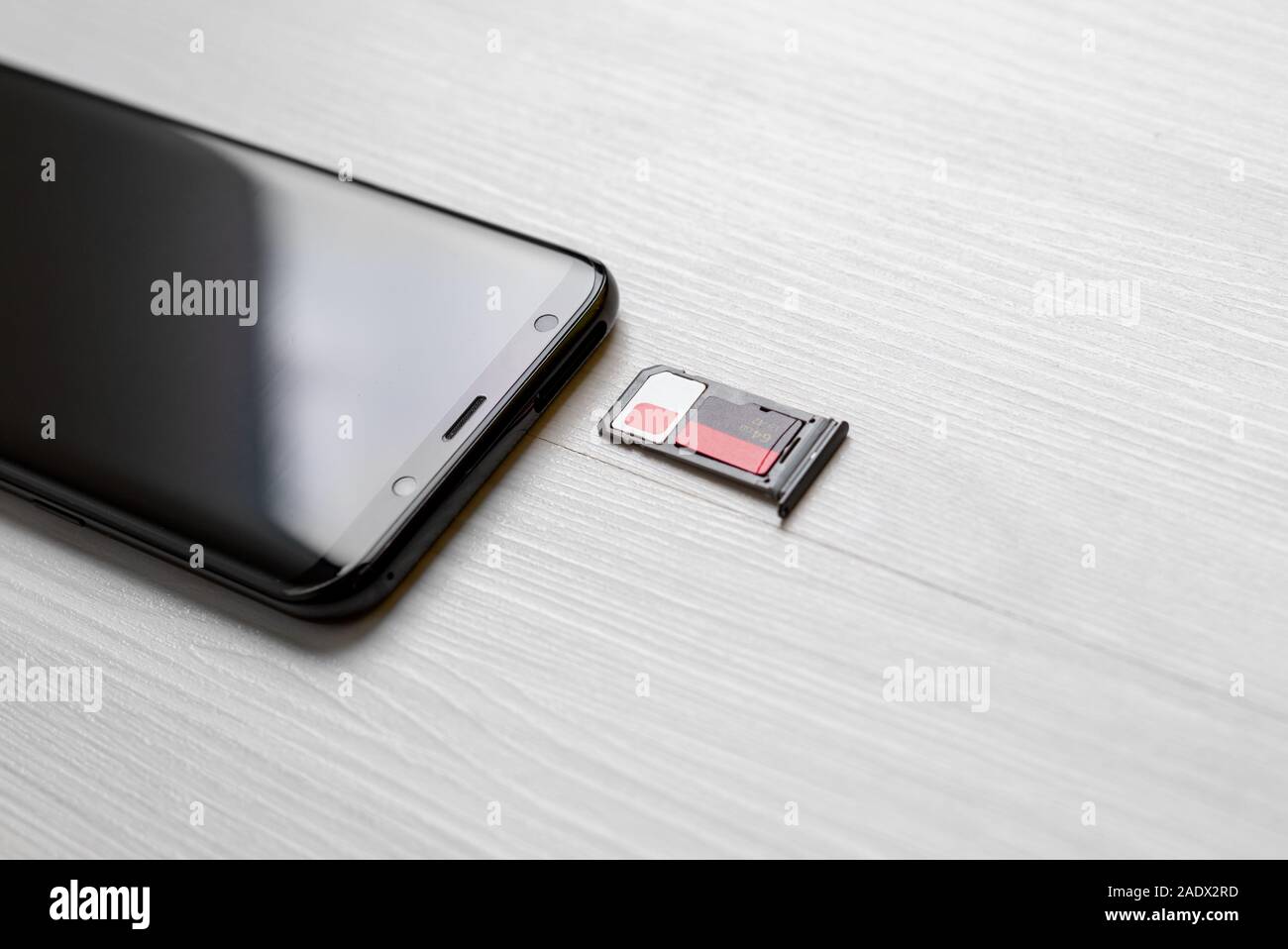 Scheda SIM e la scheda di memoria nell'adattatore accanto a smart phone sulla scrivania di close-up Foto Stock