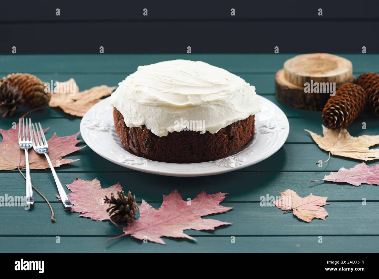 Cioccolato artigianale torta alla frutta con crema di formaggio decorato con foglie secche e coni su sfondo blu scuro Foto Stock