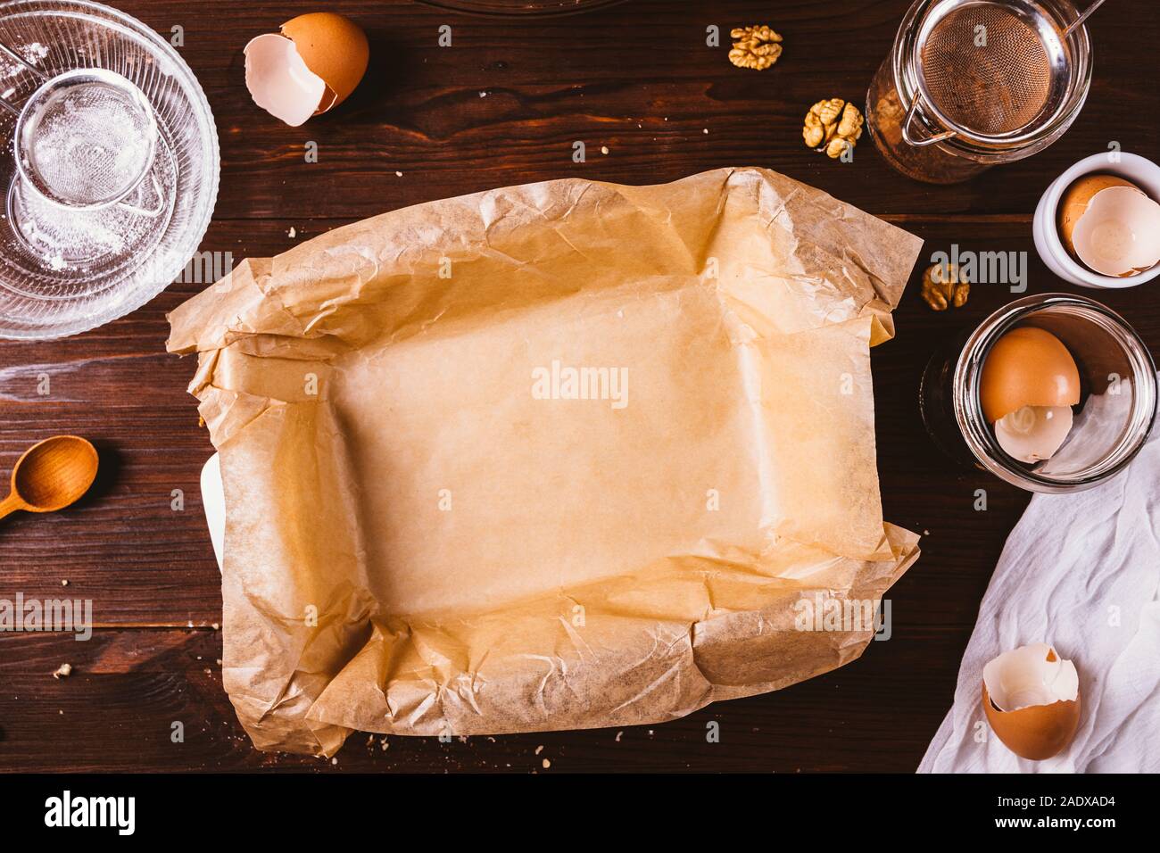 Sfruttando appieno la teglia coperta con carta pergamena su rustiche in legno scuro sfondo tra ingredienti e utensili per la produzione di pasticceria. Foto Stock