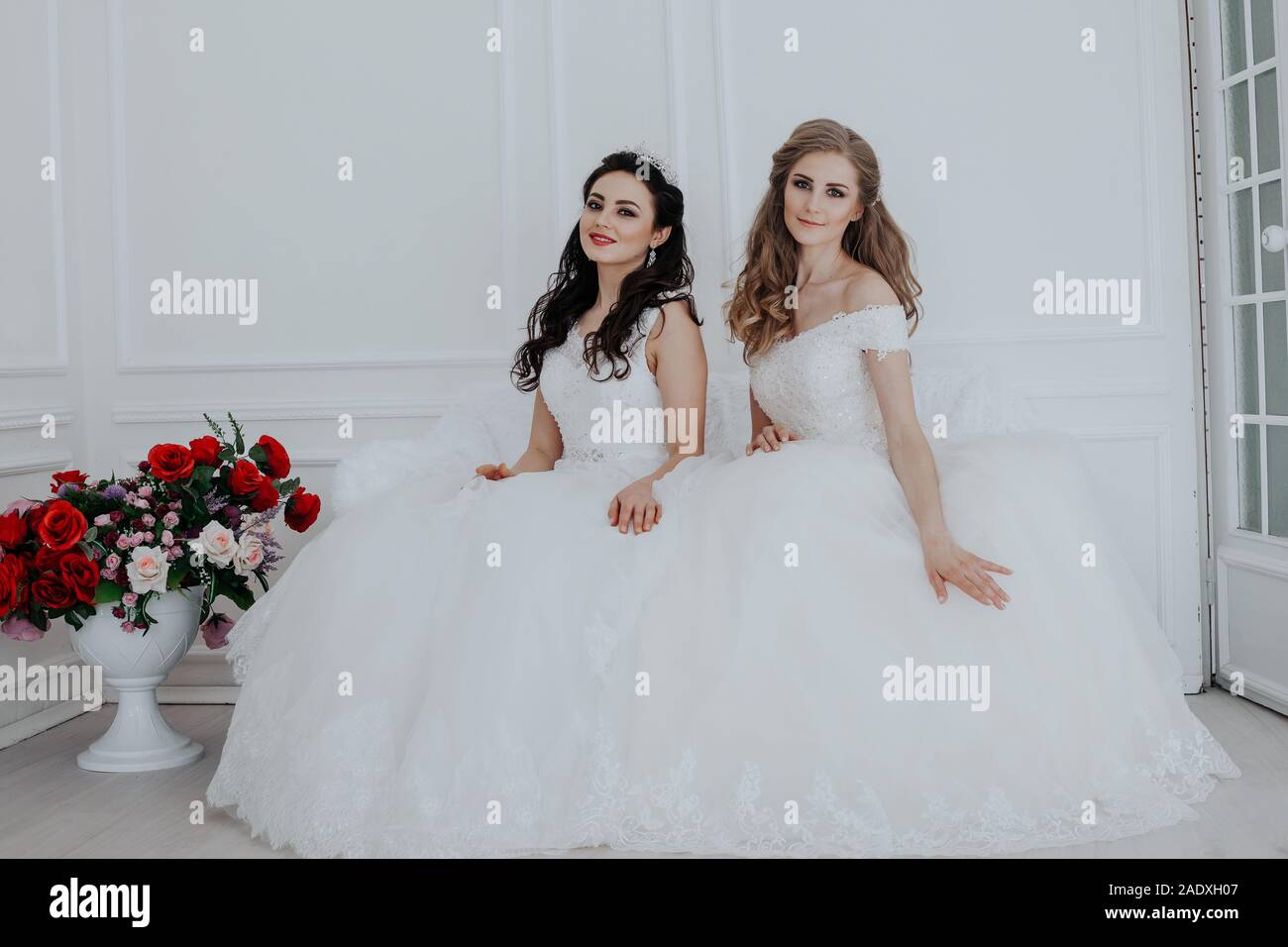 Due spose in abiti da sposa a sedersi su un divano bianco Foto stock - Alamy