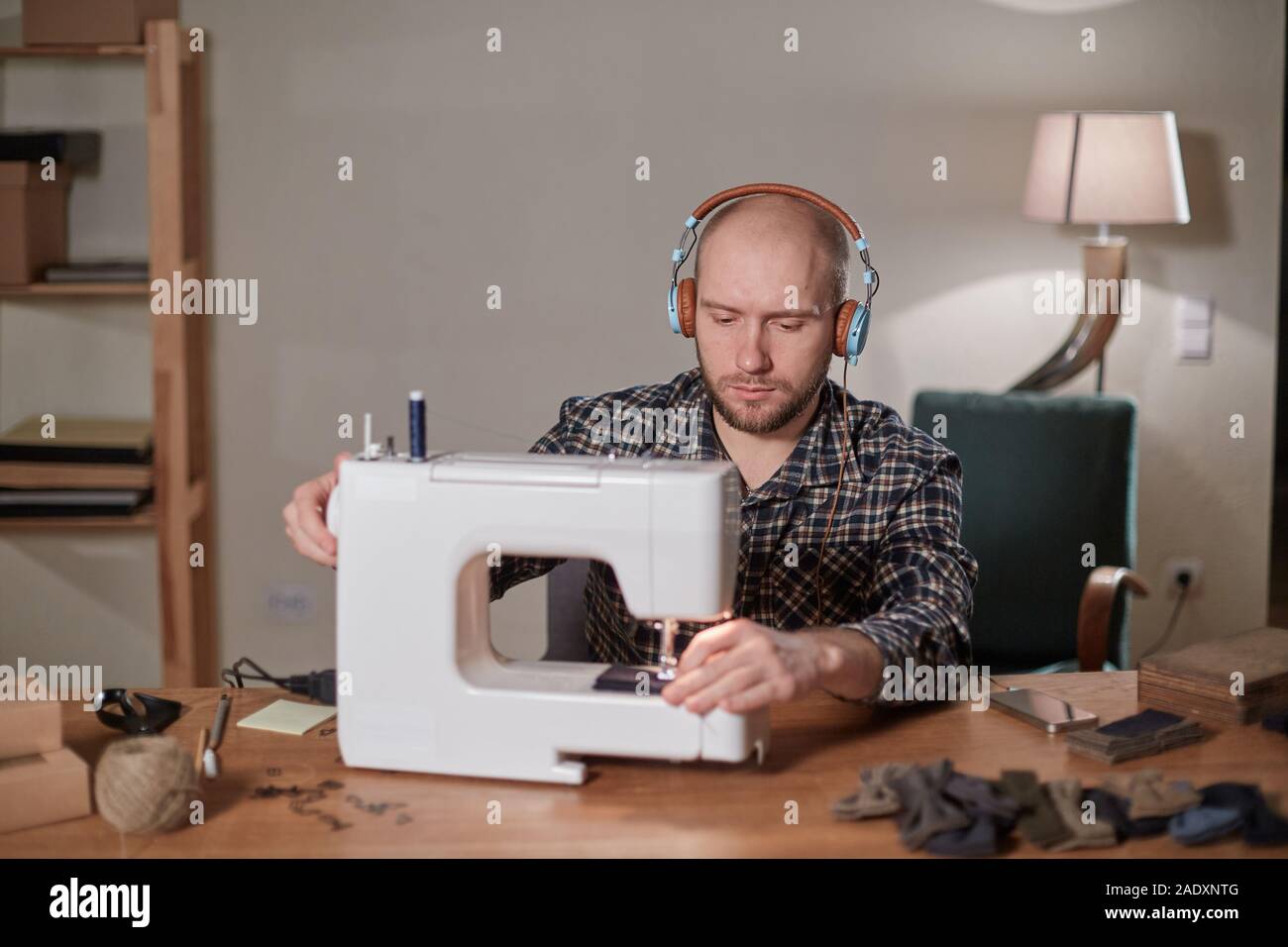 L'uomo ascoltare musica e lavorare con la macchina da cucire in un studio  di tessili. Personalizzare rende cravatte di tessuto di lana Foto stock -  Alamy