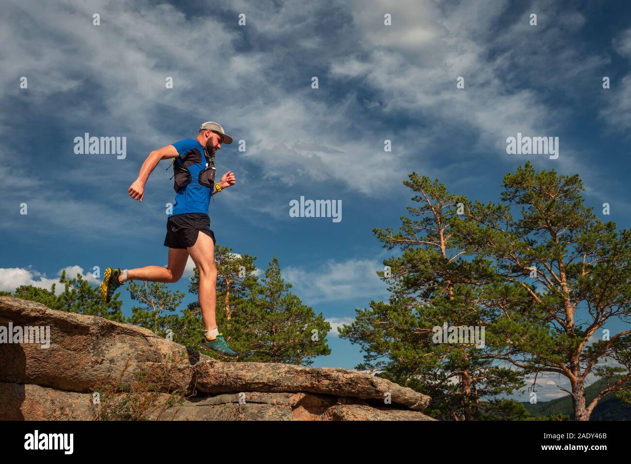 Runner maschio in esecuzione su di un sentiero di montagna. Atleta corre lungo il bordo della roccia. Uomo in maglia blu e pantaloncini neri all'aperto di formazione Foto Stock