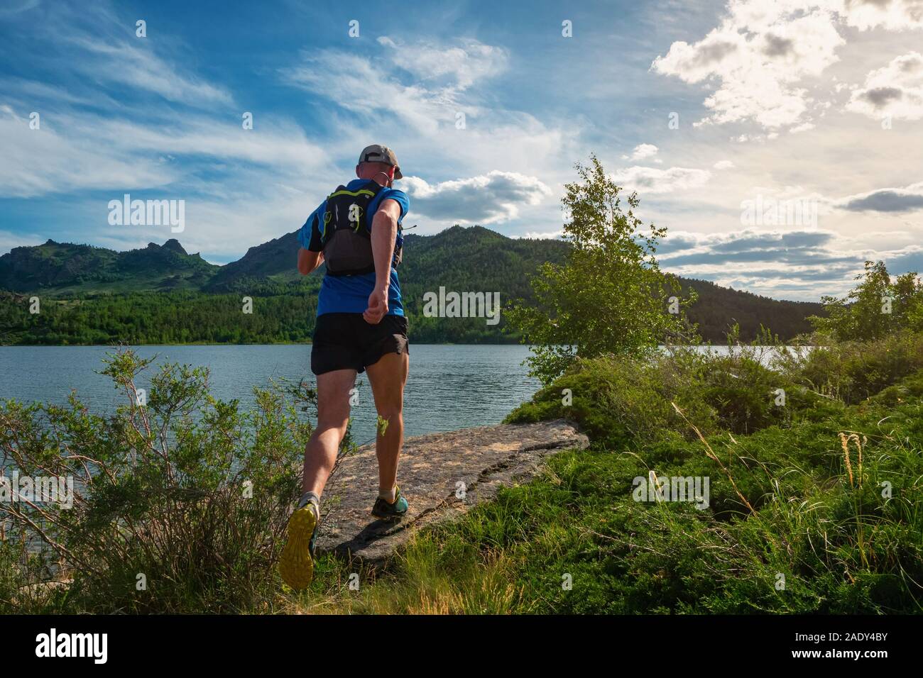 Runner maschio in esecuzione su di un sentiero di montagna. Treni atleta dal lago di montagna. Vista posteriore. Uomo in maglia blu e pantaloncini neri all'aperto di formazione Foto Stock