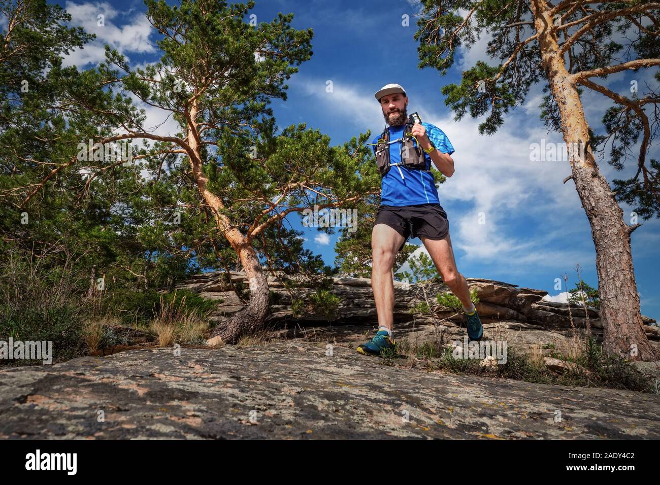 Runner maschio in esecuzione su di un sentiero di montagna. Uomo in maglia blu e pantaloncini neri della formazione all'aperto in una giornata di sole Foto Stock