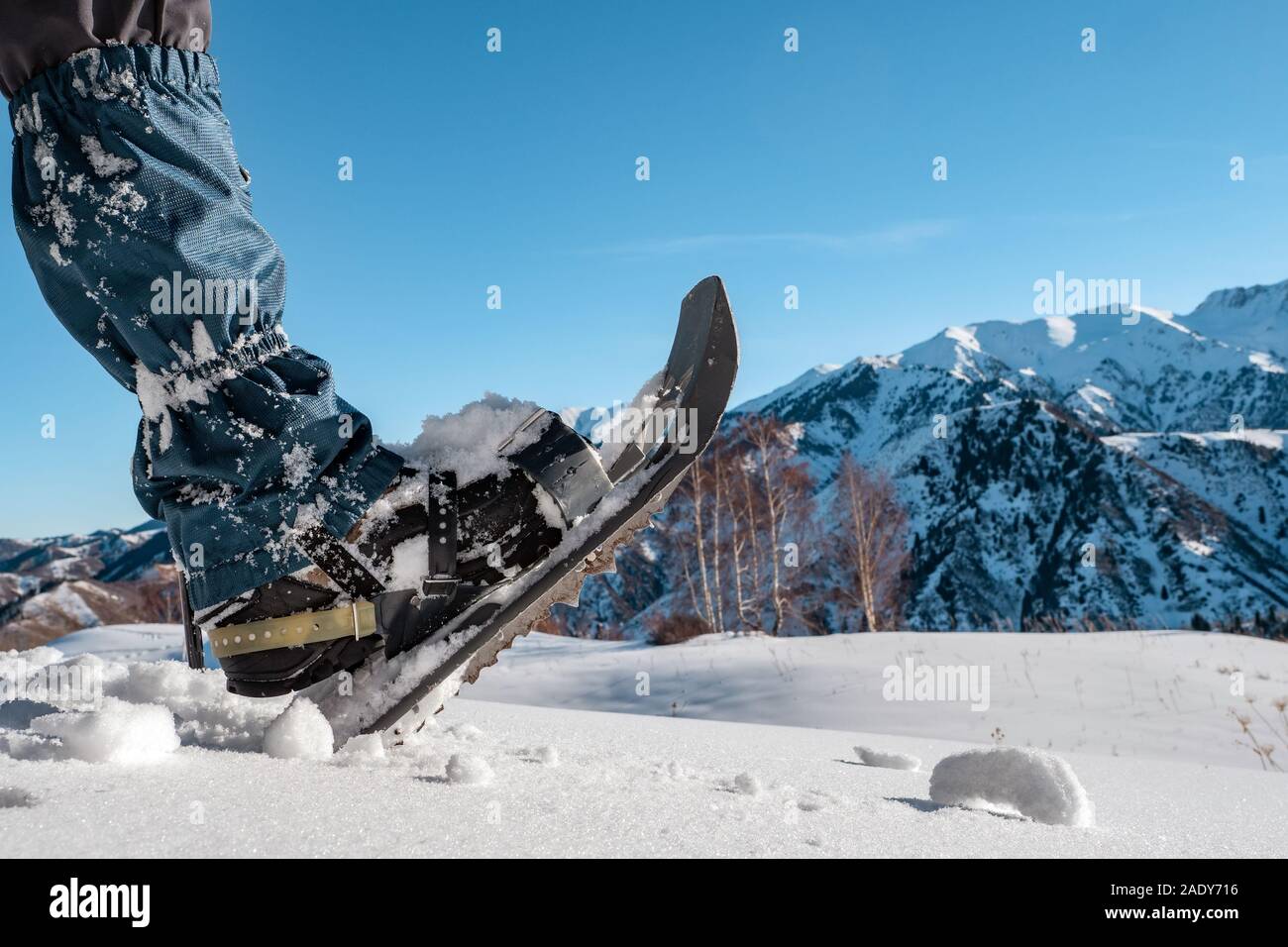 Racchette da neve indossato sulla gamba closeup sullo sfondo di montagne innevate. In inverno il turismo di montagna. Foto Stock