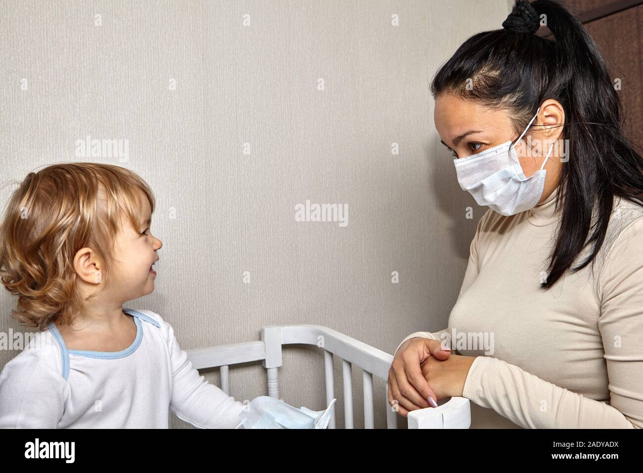 Poco carino bianco ragazza caucasica circa 2 anni sta guardando il suo mather medico con la maschera sul volto come protezione da infezioni durante illne Foto Stock