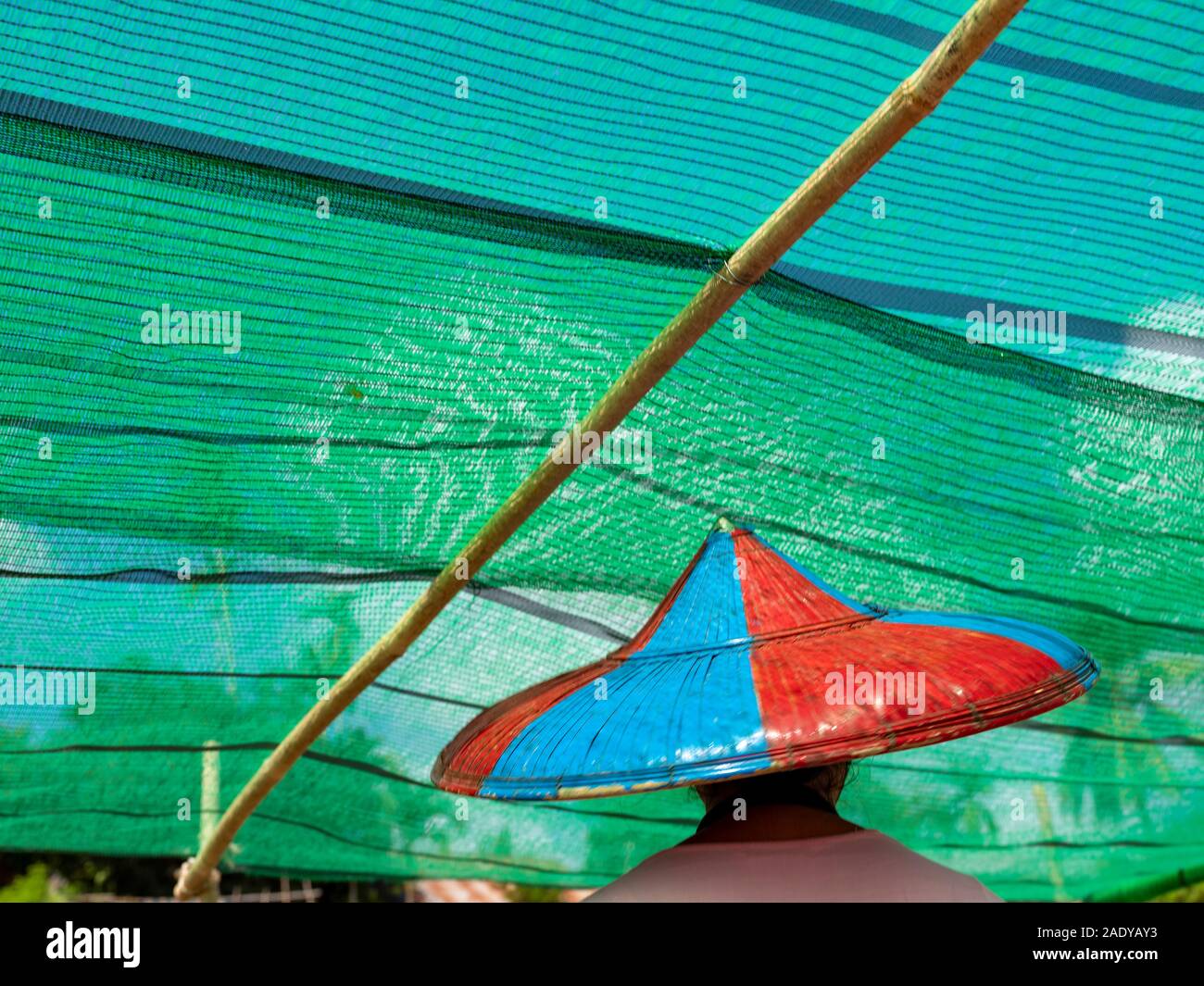 Donna birmano in un riso conica hat dipinte di rosso e blu esce un traghetto barca sotto il colore turchese sunscreen sul ponte principale sul fiume Chindwin Foto Stock