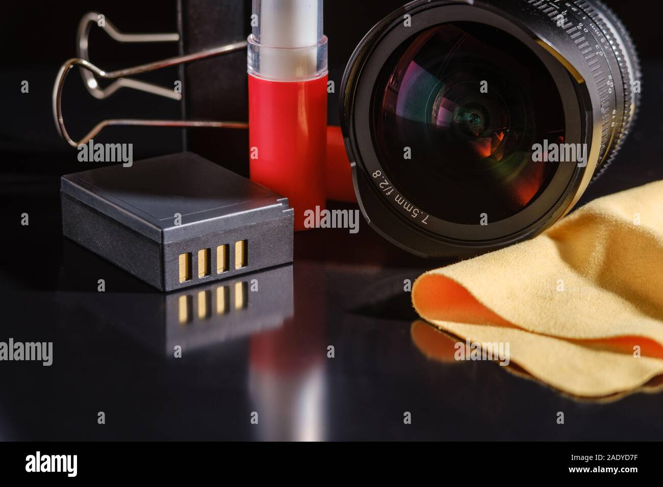 Accessori fotografici al buio su un tavolo. obiettivo, batteria e la spazzola di pulizia con un tovagliolo in microfibra. Foto Stock