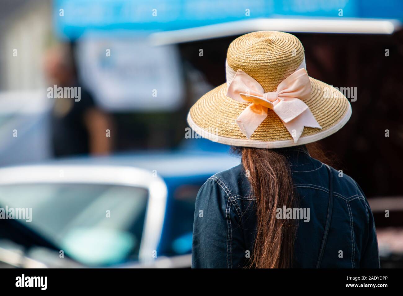 Vista posteriore della donna che indossa una giacca di jeans e cappello per il sole con larga tesa come si guarda a autovetture durante outdoor antique car show, torna il fuoco selettivo. Foto Stock