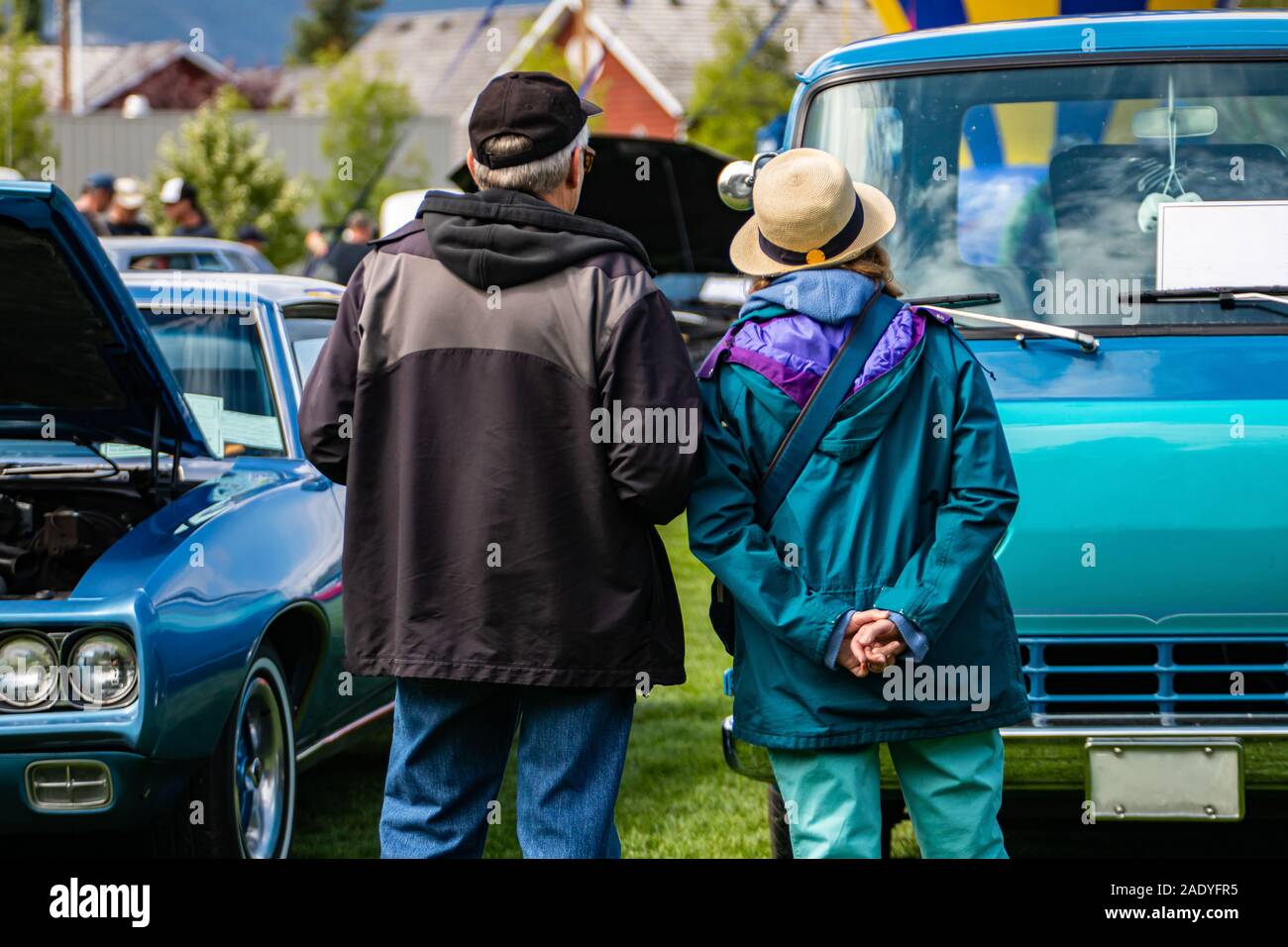 Una vista posteriore di una vecchia coppia guardando classic cars, durante un outdoor antique car show, sport muscolo, e blu van vetture nella parte anteriore di essi Foto Stock