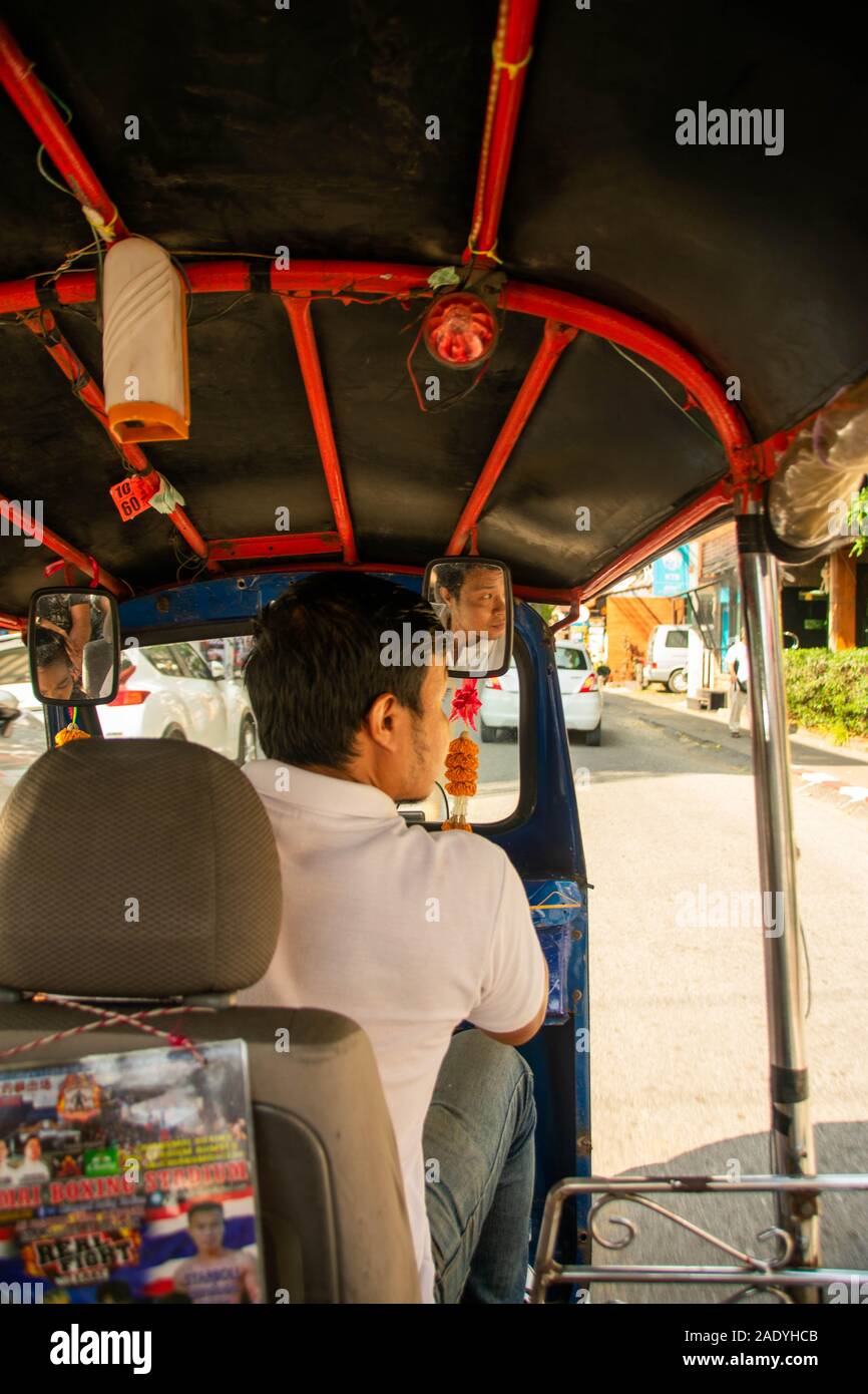 Un uomo alla guida di un rosso tuk tuk per le strade della città di Chiang Mai in Thailandia Foto Stock