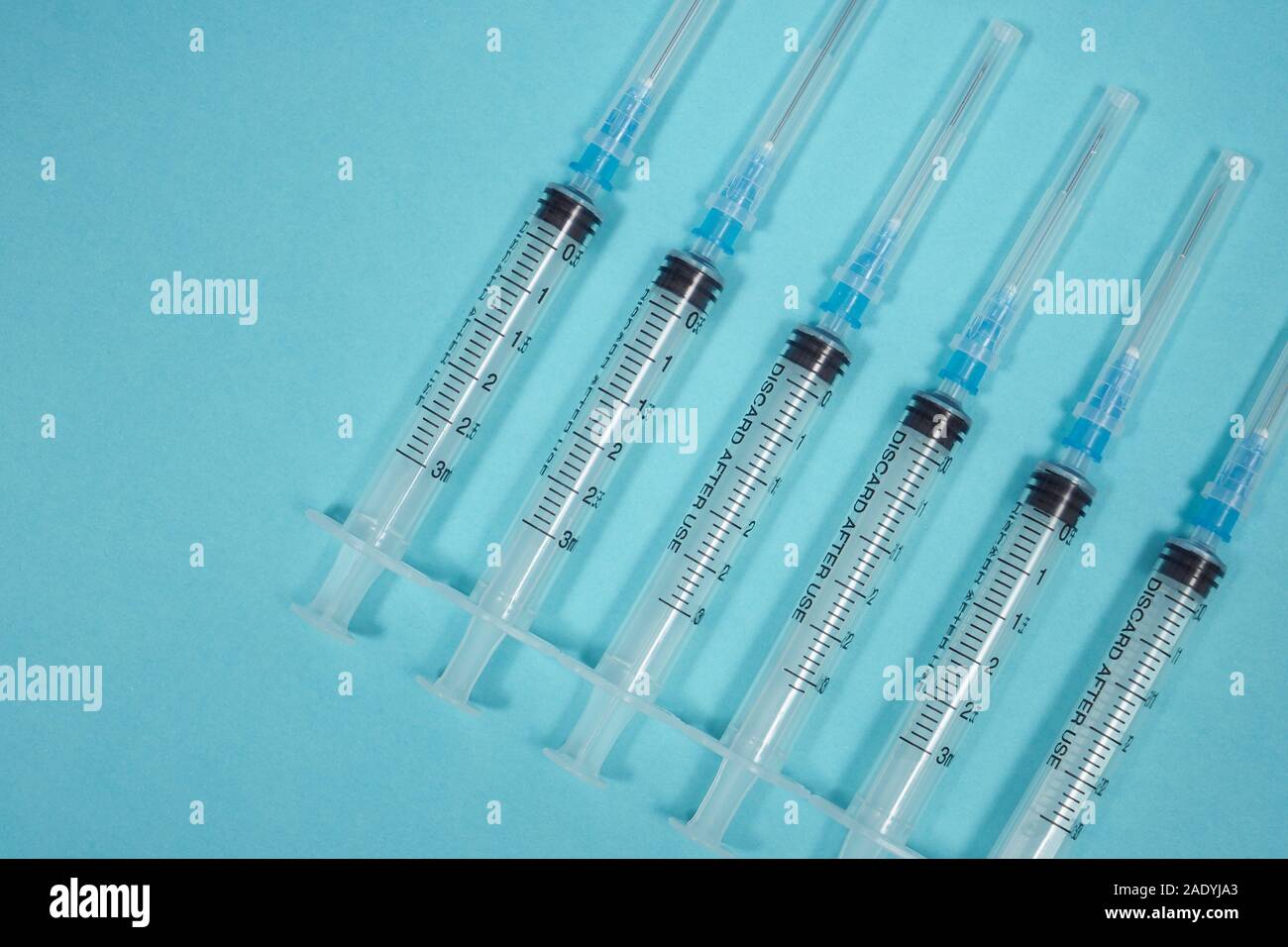 Sei siringhe vuote in fila su sfondo turchese. Background medico. Un ciclo di trattamento per un paziente. Concetto di tossicodipendenza. Coronavirus. Foto Stock