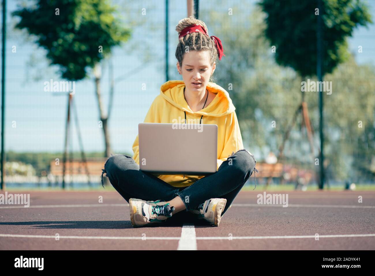 Grave giovane donna di indossare un abbigliamento informale e avente laptop sulle ginocchia Foto Stock