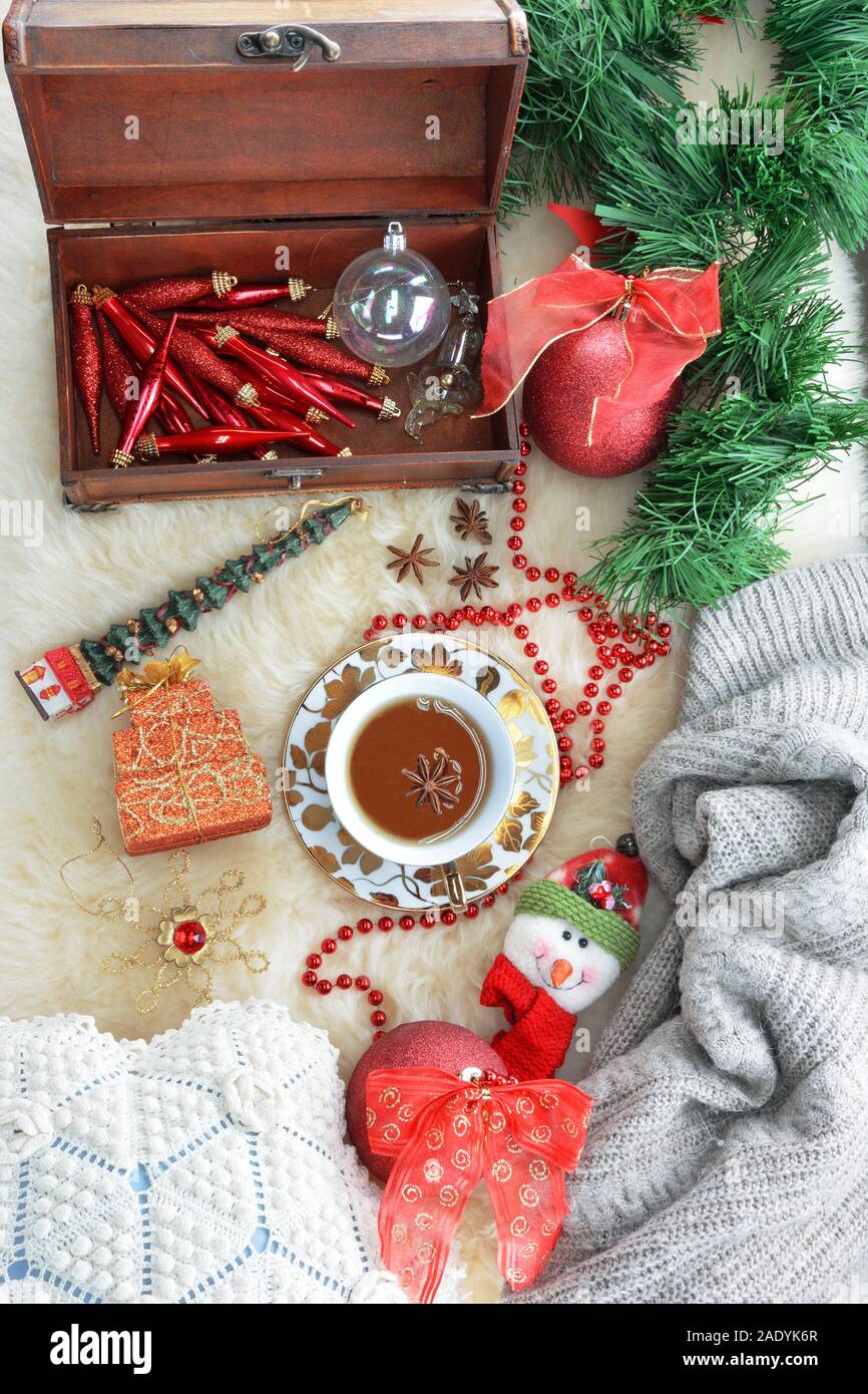 Τea cup con abbinamento di piattino,stelle anice, ornamenti Natale , una scatola di legno con ornamenti ,un maglione e un cuscino sul tappeto di pelle di pecora Foto Stock