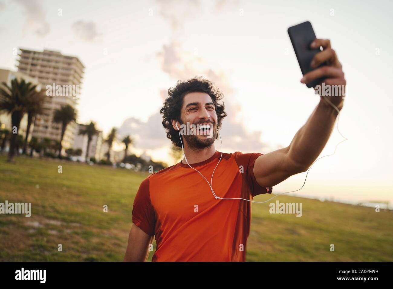Sorridente ritratto di un caucasian montare giovane uomo con gli auricolari nelle orecchie rendendo la chiamata video da smart phone dopo esercizio nel parco - Giovane maschio Foto Stock