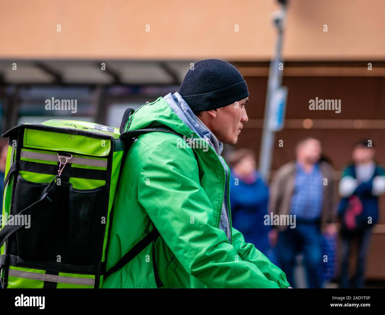 Mosca, Russia - 19 Ottobre 2019: Servizi di corriere di etnia asiatica in uniforme e di marca Consegna verde club zaini con la bici su strada. Busta termica Foto Stock