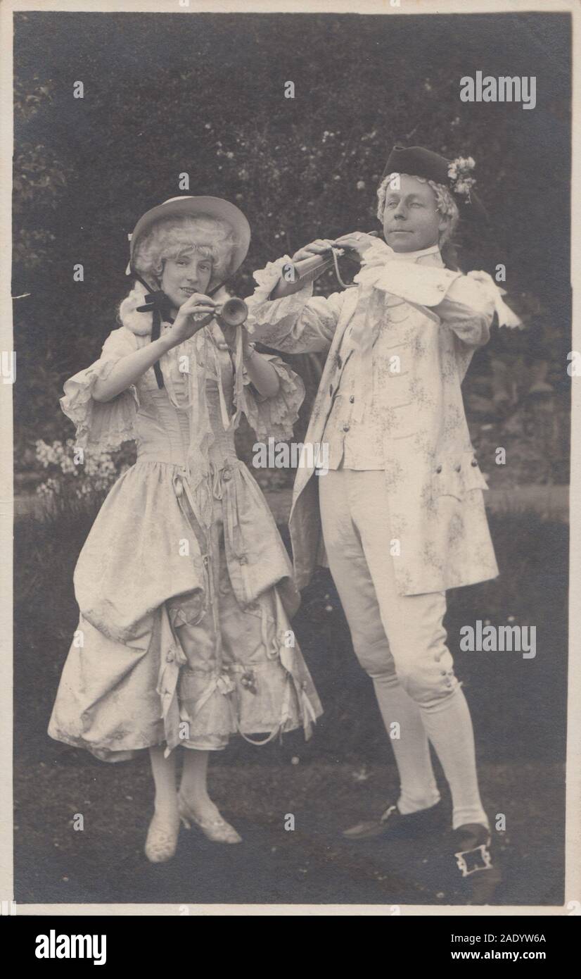 Vintage Cartolina fotografica che mostra un uomo e una donna che indossano costumi teatrali suonare uno strumento musicale. Foto Stock