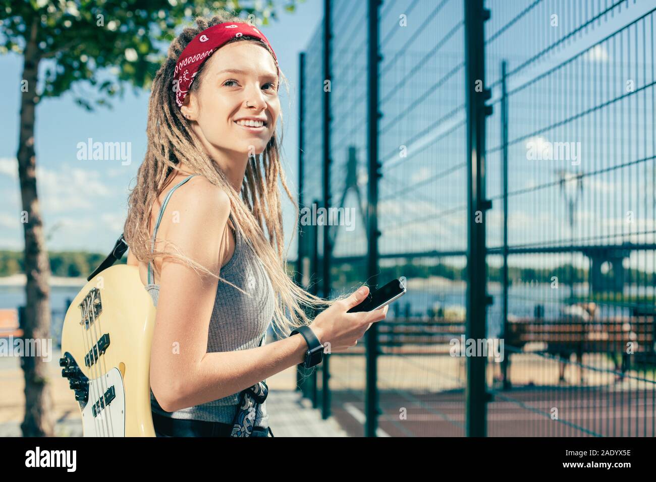 Signora emotiva sorridente mentre si sta portando la sua chitarra e lo smartphone Foto Stock