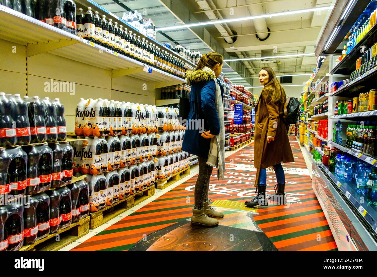 Due giovani donne tra gli scaffali dei supermercati, il reparto bevande presso gli scaffali del supermercato Tesco, con vista su tutto il negozio, non hanno prezzo Foto Stock