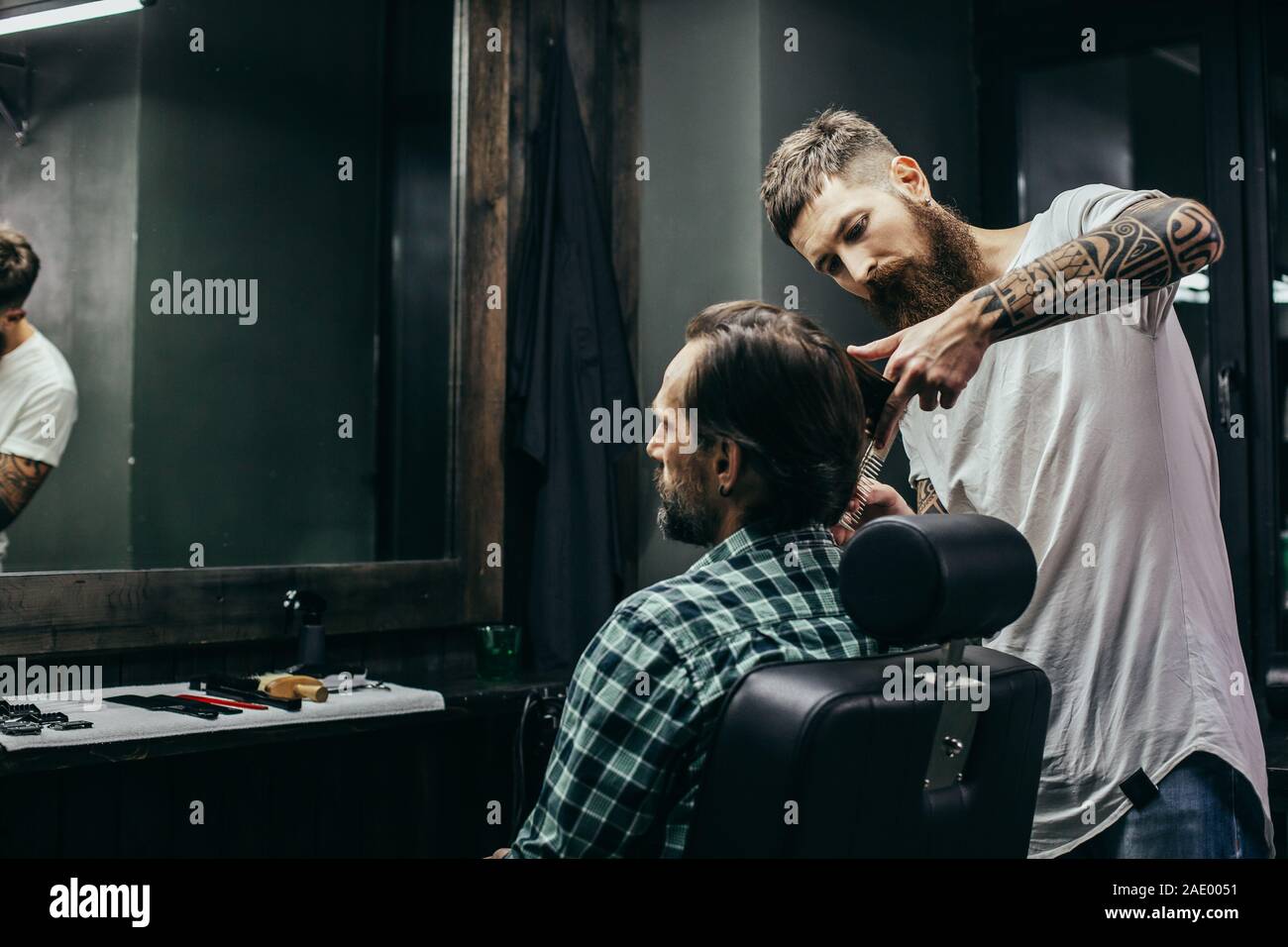Barbiere concentrato in piedi vicino al client e il suo taglio di capelli Foto Stock