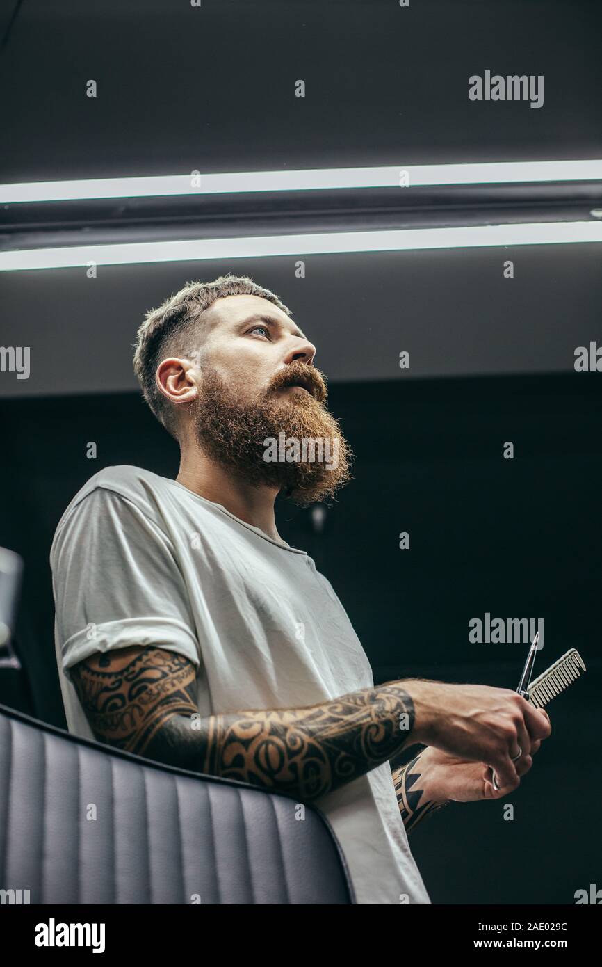 Grave uomo barbuto azienda strumenti da barbiere e guardando in lontananza Foto Stock