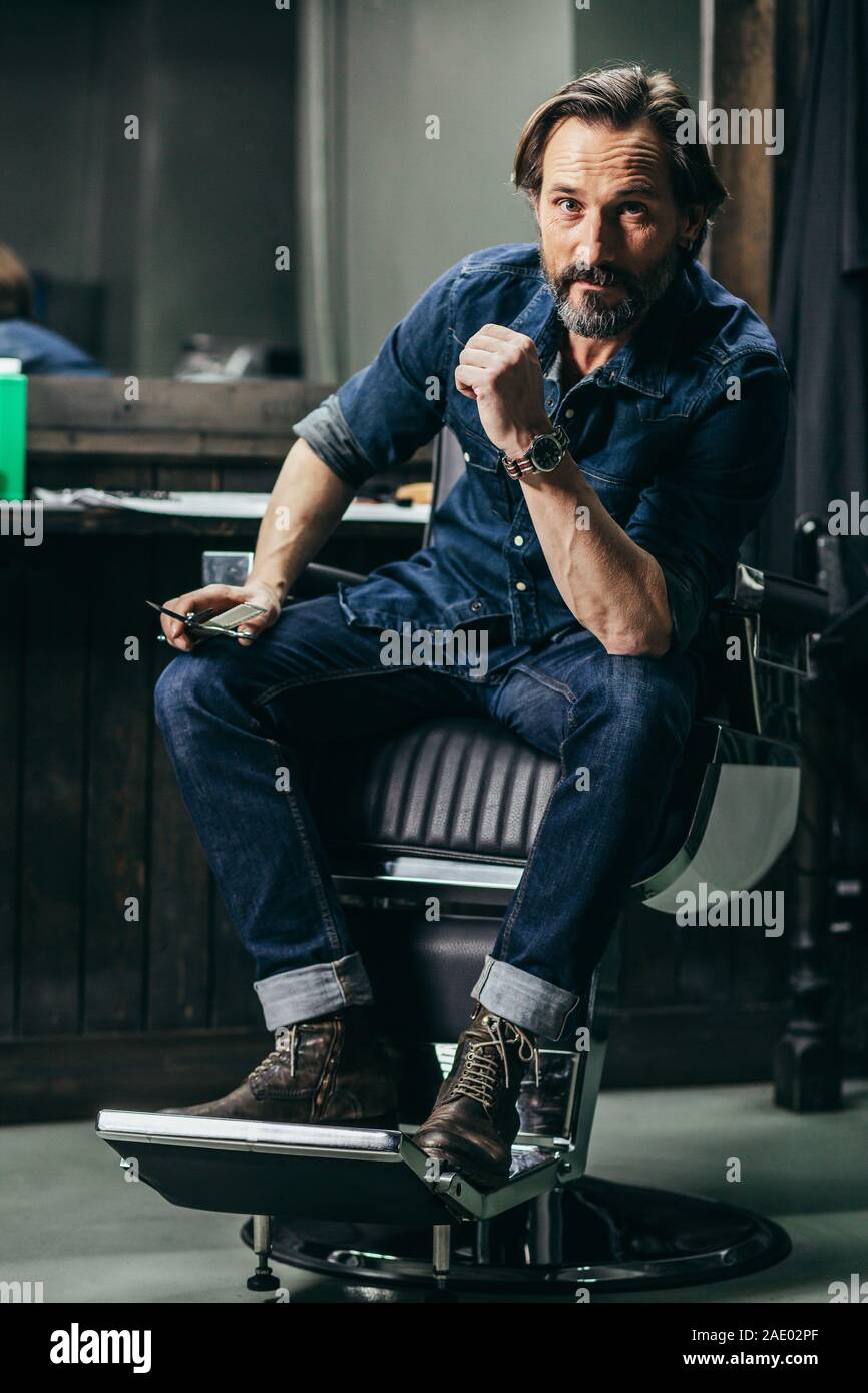 Fiducioso uomo mettendo il gomito sul ginocchio durante il posizionamento in un barbiere Foto Stock