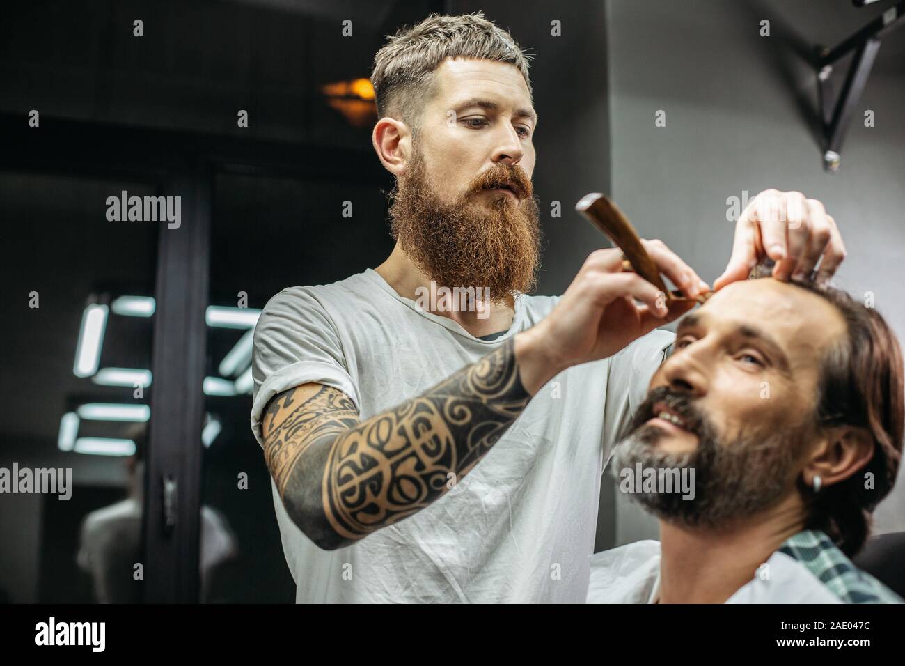 Attento barbiere guardando i capelli di client mentre si lavora con il rasoio Foto Stock