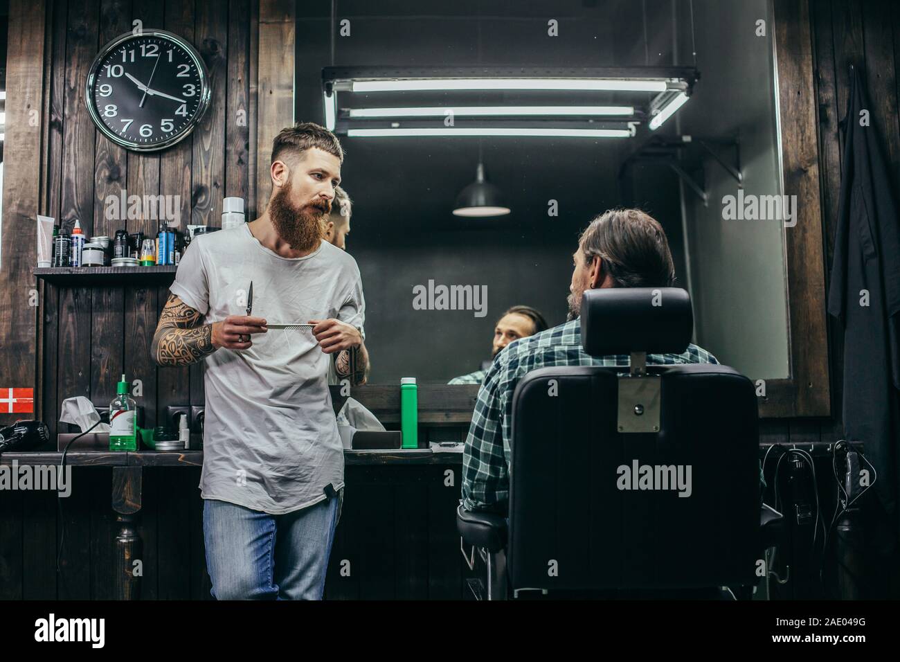 Dai capelli scuri uomo seduto in poltrona e guardando il barbuto barbiere Foto Stock