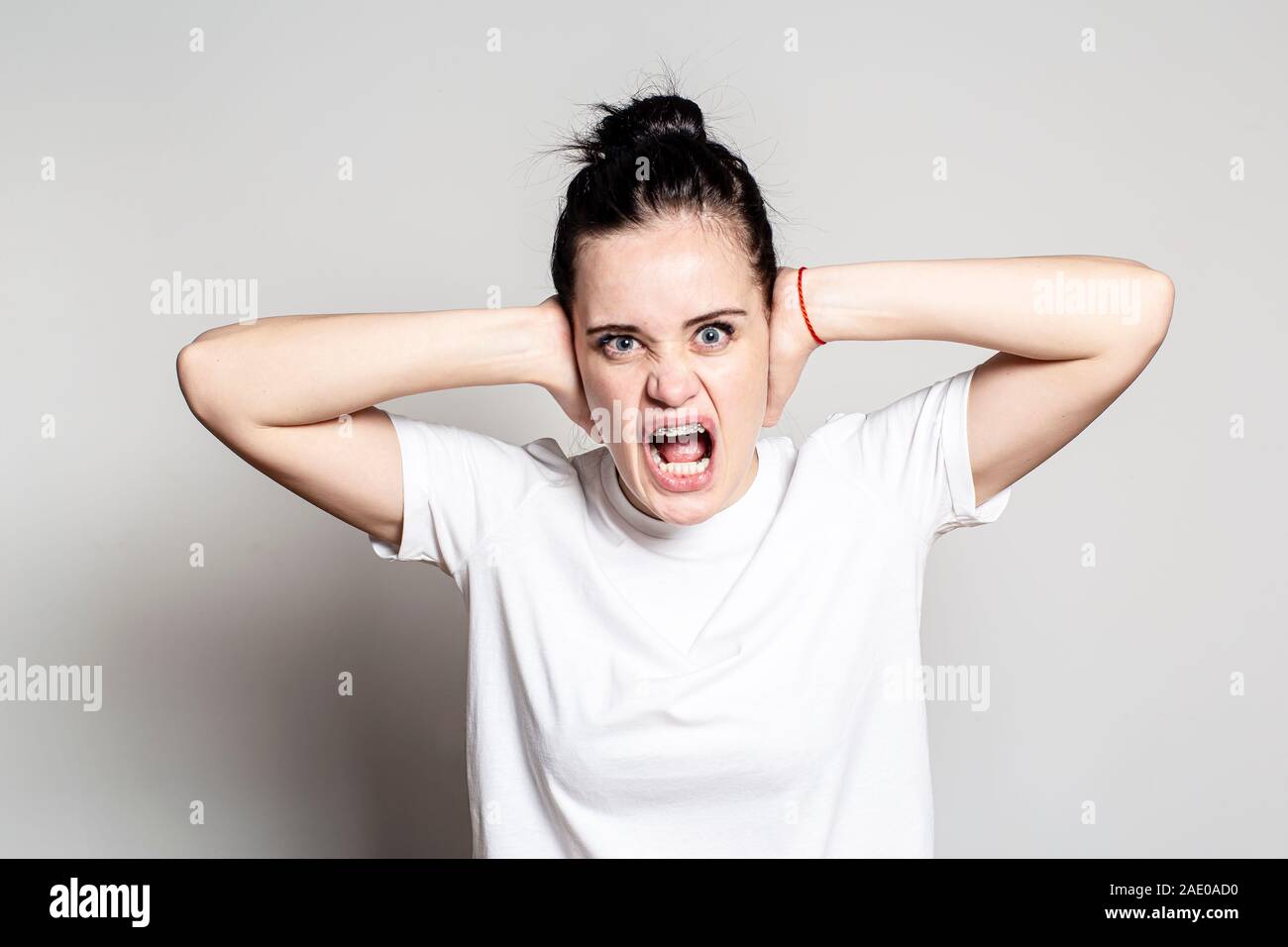 La donna è furiosa. Ella ha coperto le sue orecchie con le mani, aprì la bocca e urla ad alta voce, guardando con odio verso la telecamera. Le emozioni negative. Foto Stock