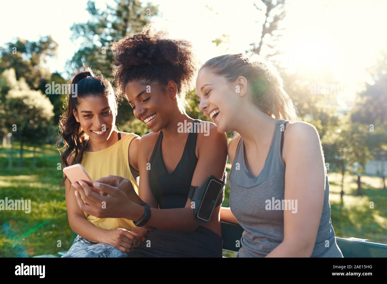 Donna sorridente diversi amici guardando il telefono cellulare sorridente e divertirsi al mattino presso il parco - amici ridere insieme Foto Stock