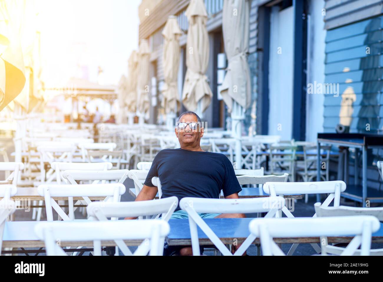 Colore blu, stile caffetteria alla moda house. Attività atletiche di anziani sorridenti uomo seduto nel ristorante. Senior proprietario di small business nel suo cafè house. Foto Stock