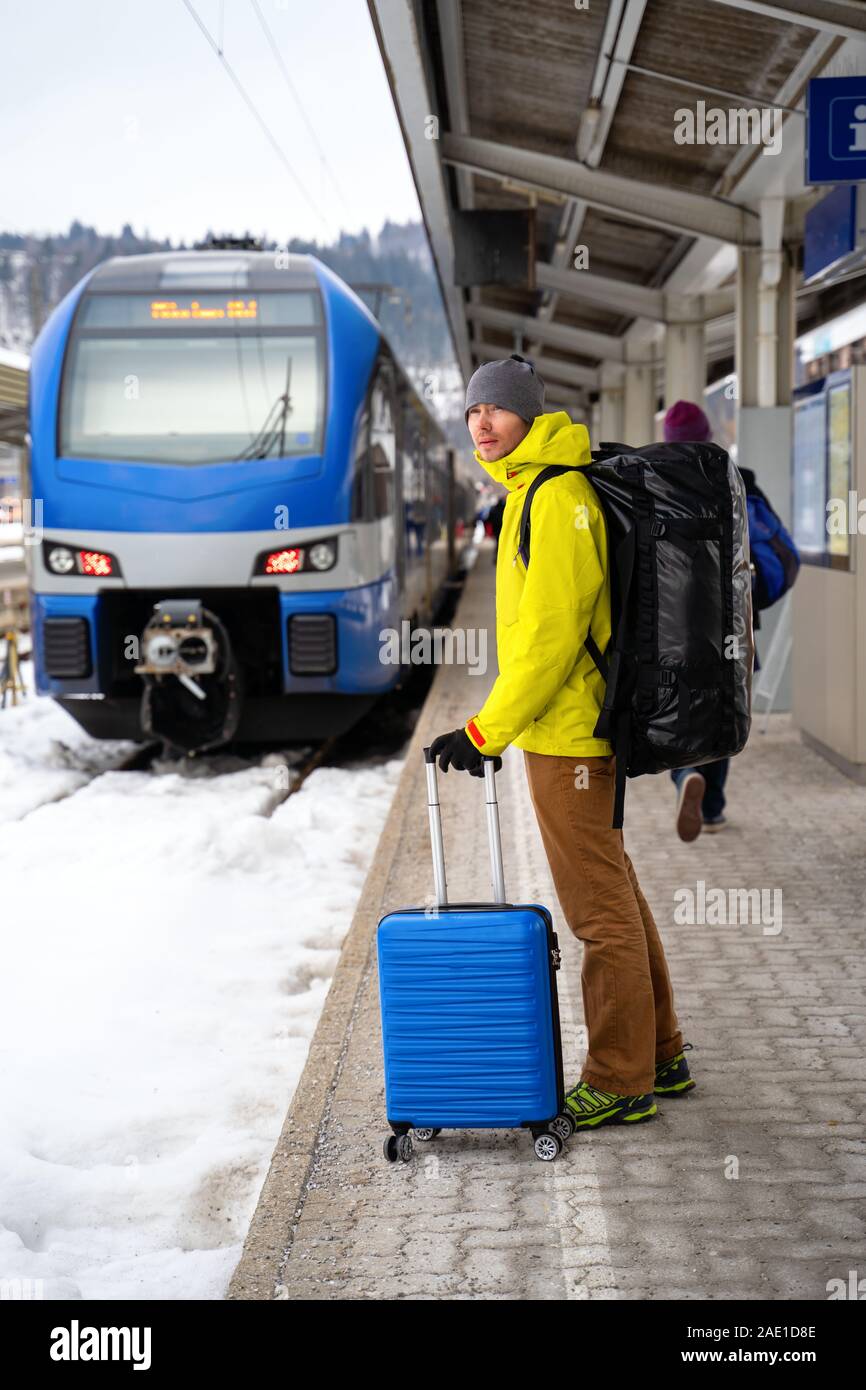 Per turisti in cerca di fotocamera con valigia blu alla stazione in attesa del treno contro sullo sfondo di montagne sulla giornata invernale Foto Stock