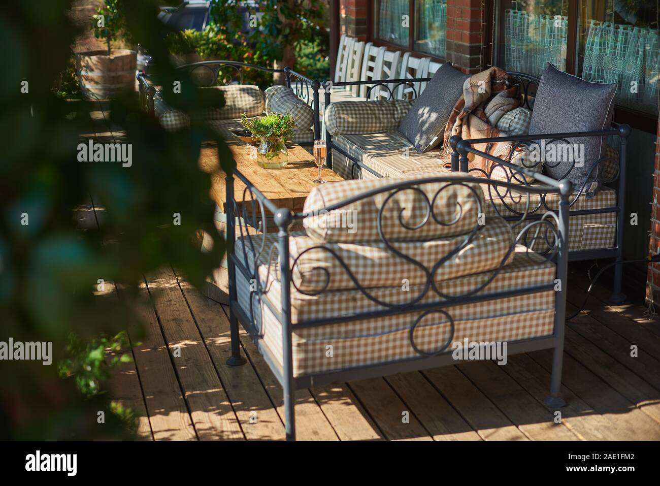 Accogliente terrazzo con divani per il riposo, il vetro con champagne su un tavolo di legno. Giornata di sole. Foto Stock