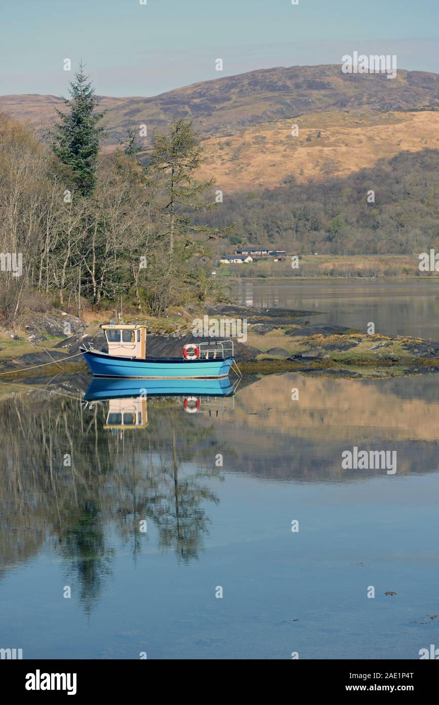 Una piccola barca da pesca riflette pacificamente nelle calme acque del Loch CRERAN, SCOZIA Foto Stock