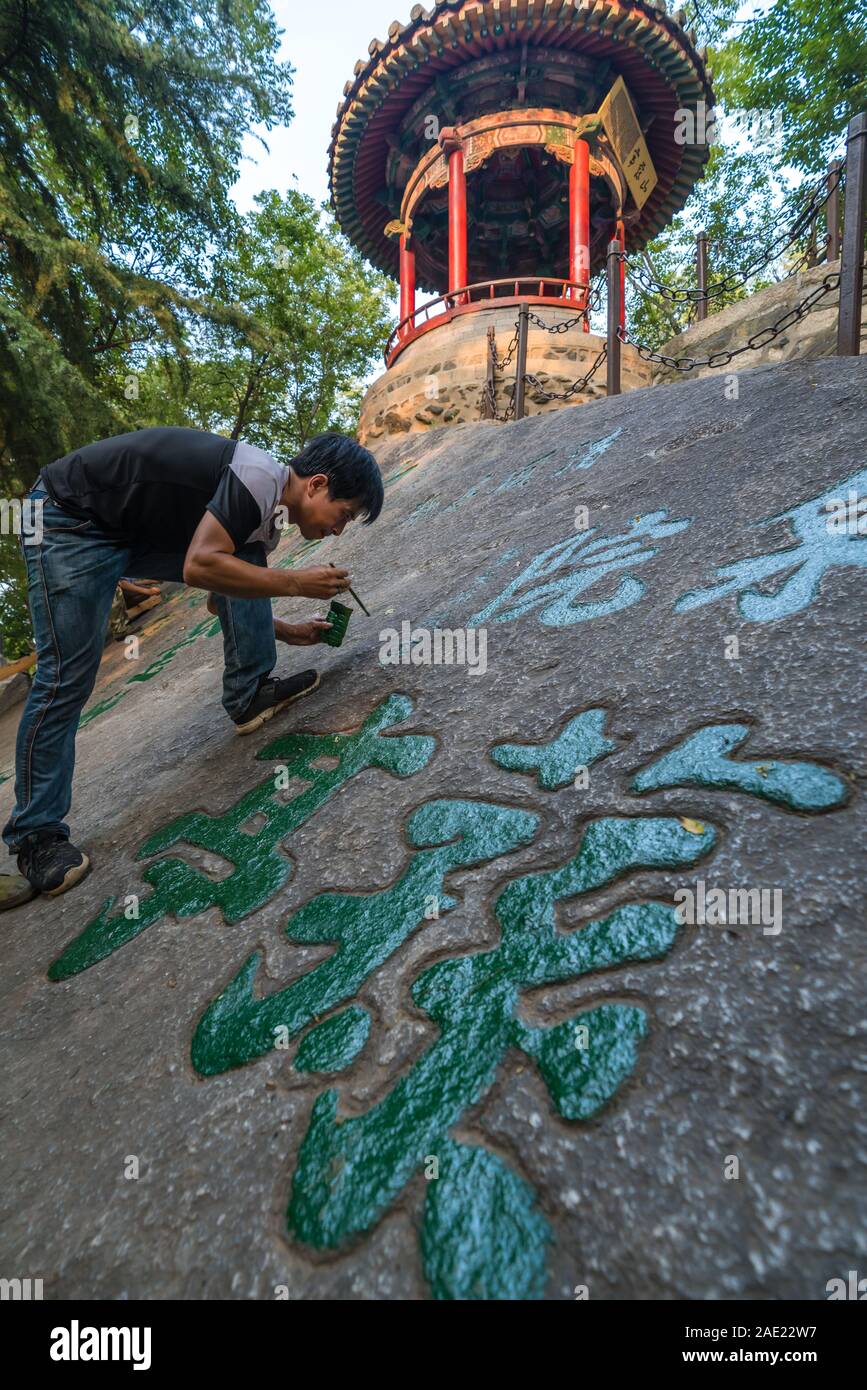 Huashan, Cina - Agosto 2019 : uomo pittura calligrafia cinese caratteri su un grande masso nel cortile di un tempio buddista ai piedi di Hu Foto Stock