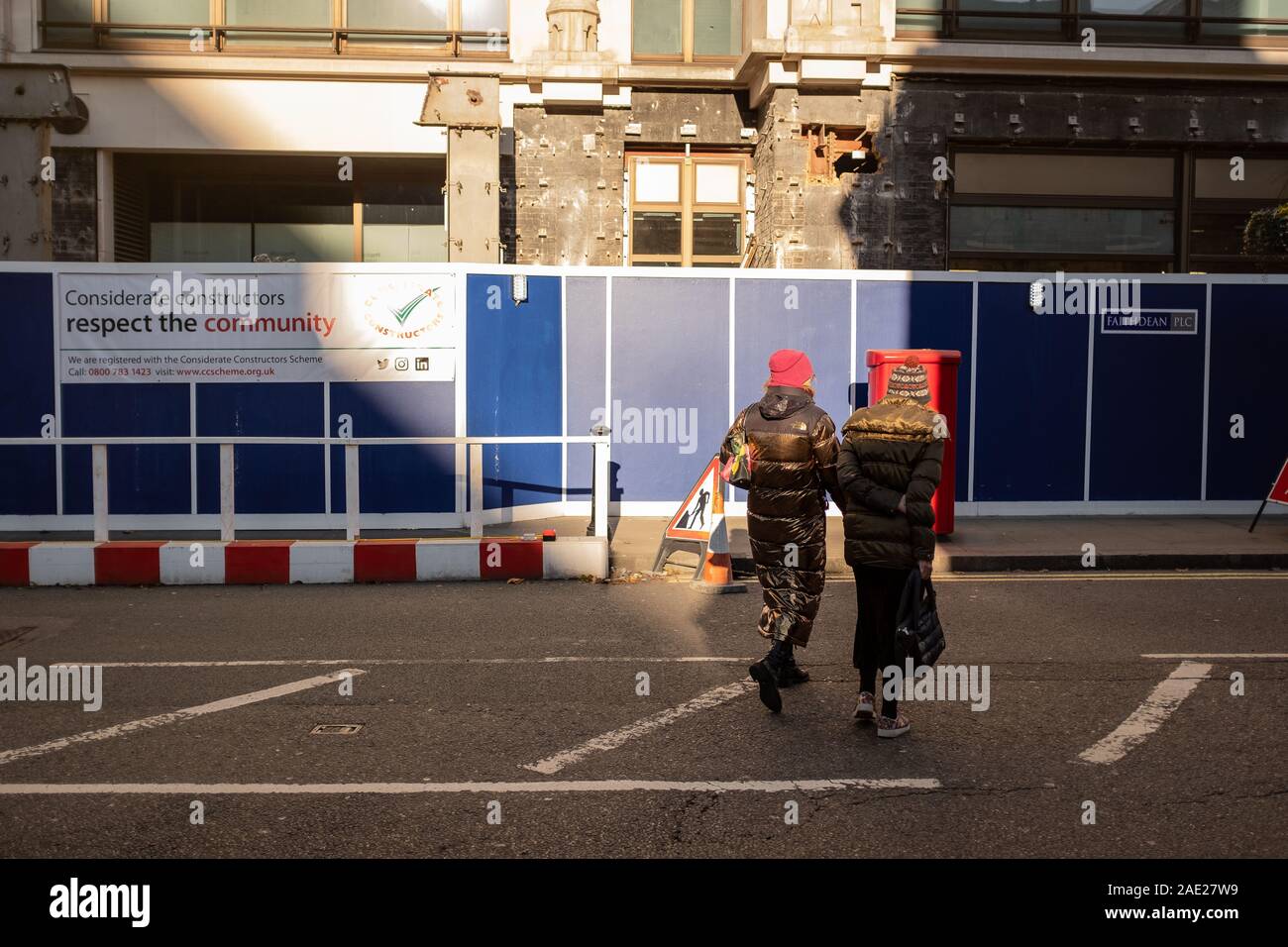 Due signore in cappotti invernali cross road verso il sito in costruzione Foto Stock