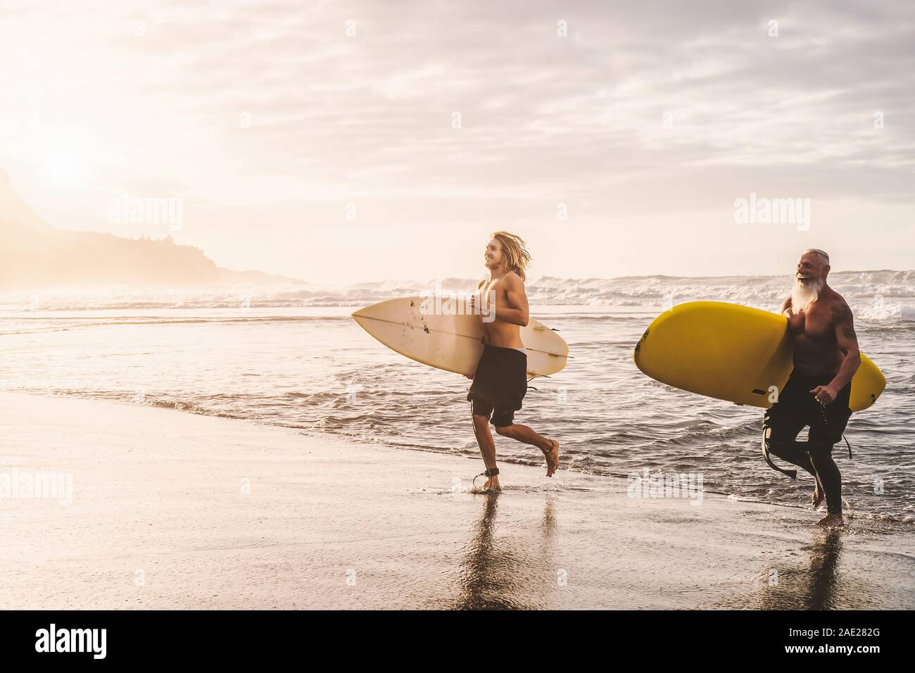 Montare felici amici divertendosi surf sul tramonto - Surfers padre e figlio in esecuzione fuori l'oceano - Sportivo lo stile di vita delle persone ed extreme sport concept Foto Stock