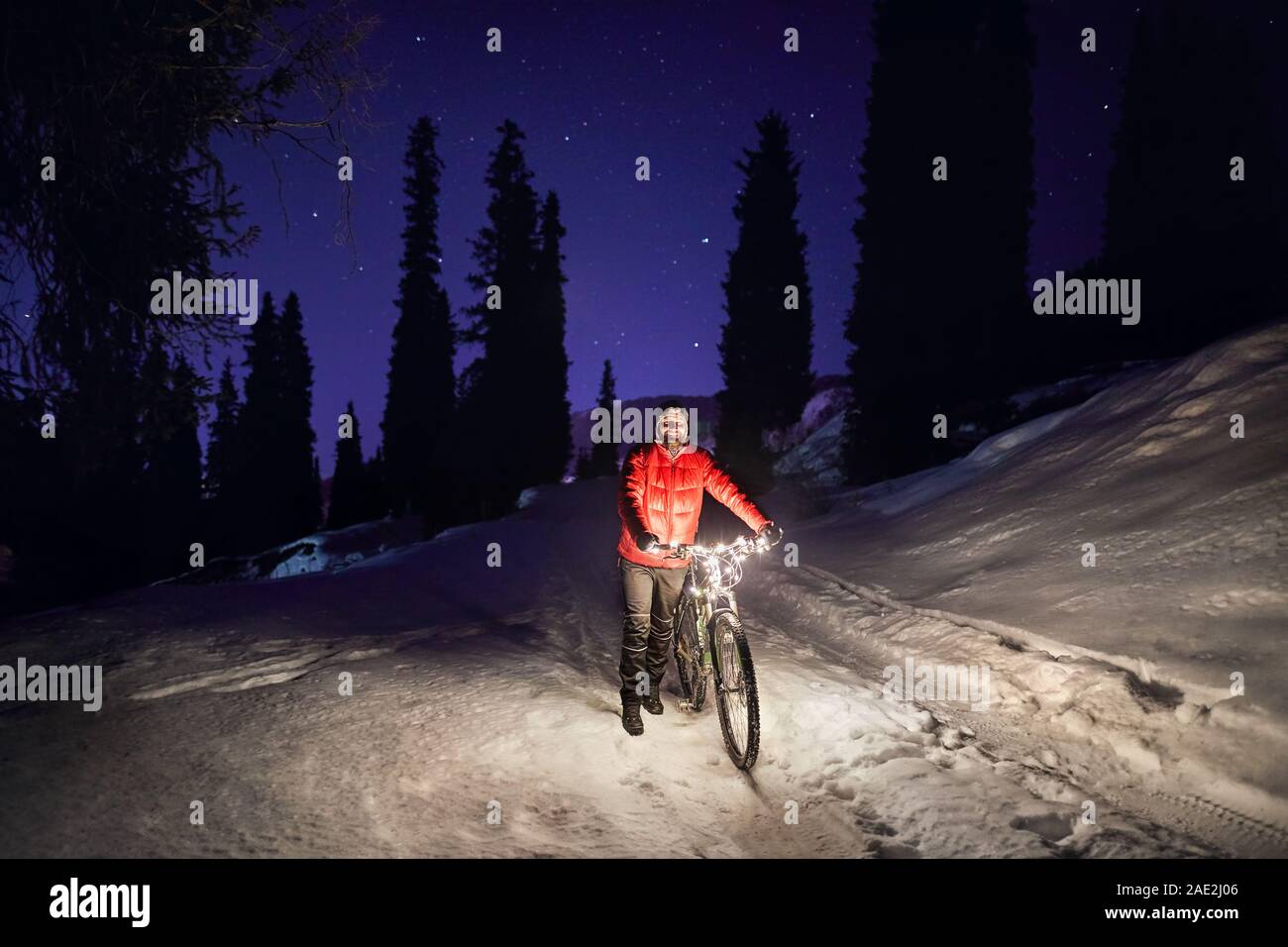Uomo in camicia rossa con la bicicletta a inverno boschi innevati in montagna sotto il cielo notturno con stelle Foto Stock