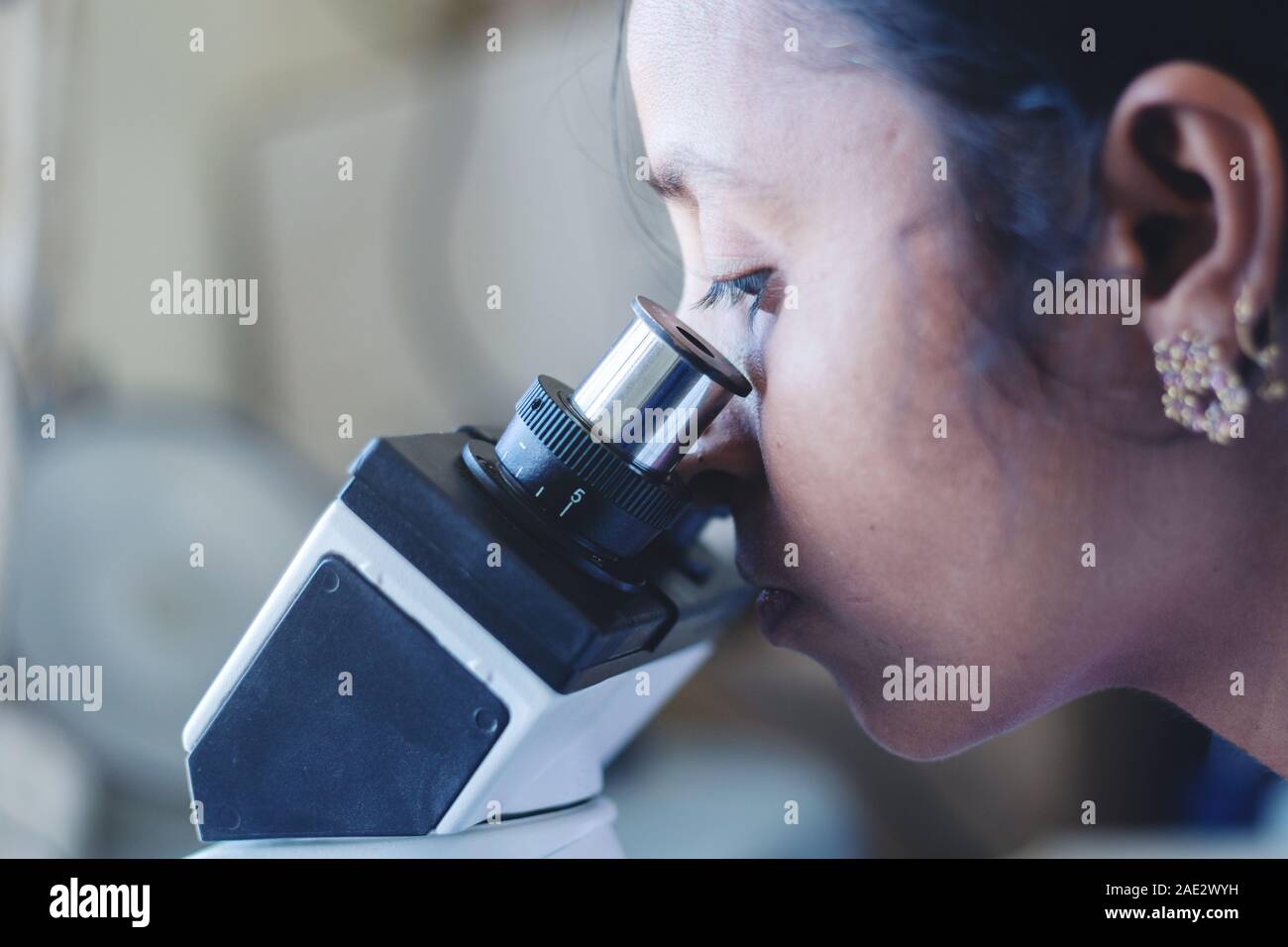 Close up della donna utilizzando un microscopio in un laboratorio - donna scienziato occupato in cerca nel microscopio. Foto Stock