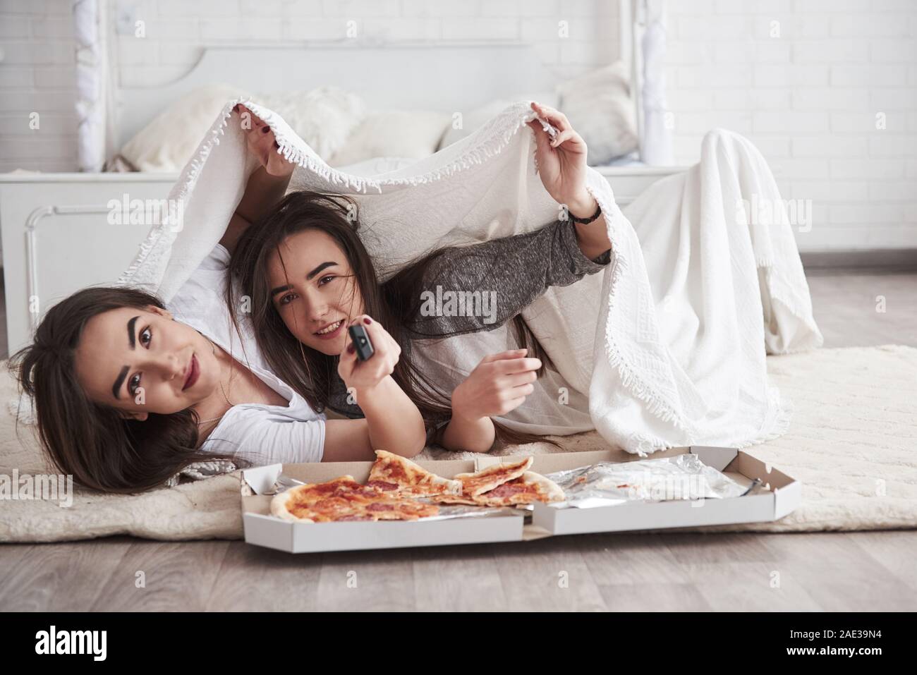 Insieme è sempre più divertente. La calda coperta. Sorelle di mangiare la pizza quando guardi la TV sdraiati sul pavimento della camera da letto Bella di giorno Foto Stock