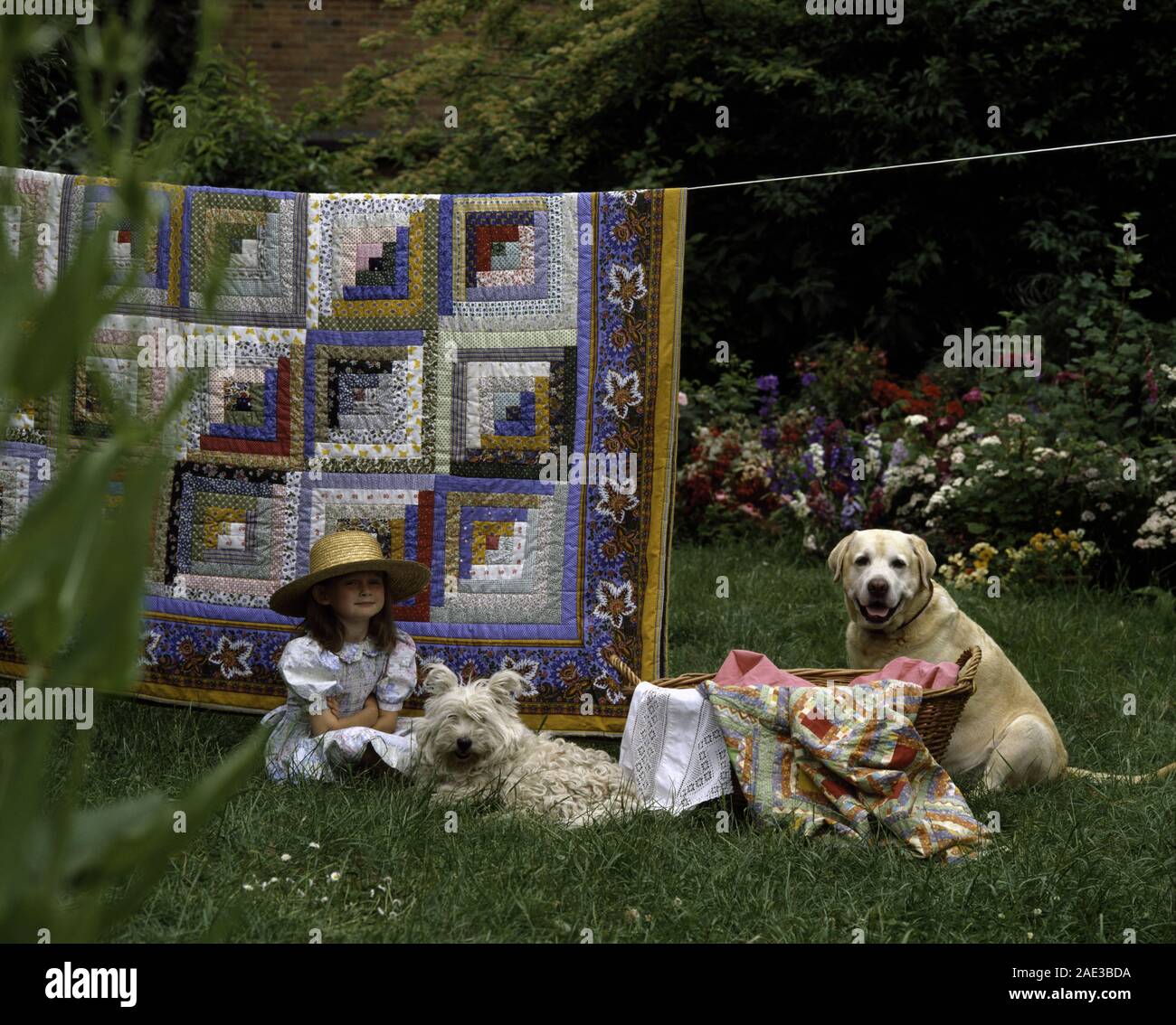 Piccola ragazza seduta con un West Highland Terrier e un Golden Labrador cane sotto un mosaico appeso sopra una linea di lavaggio Foto Stock