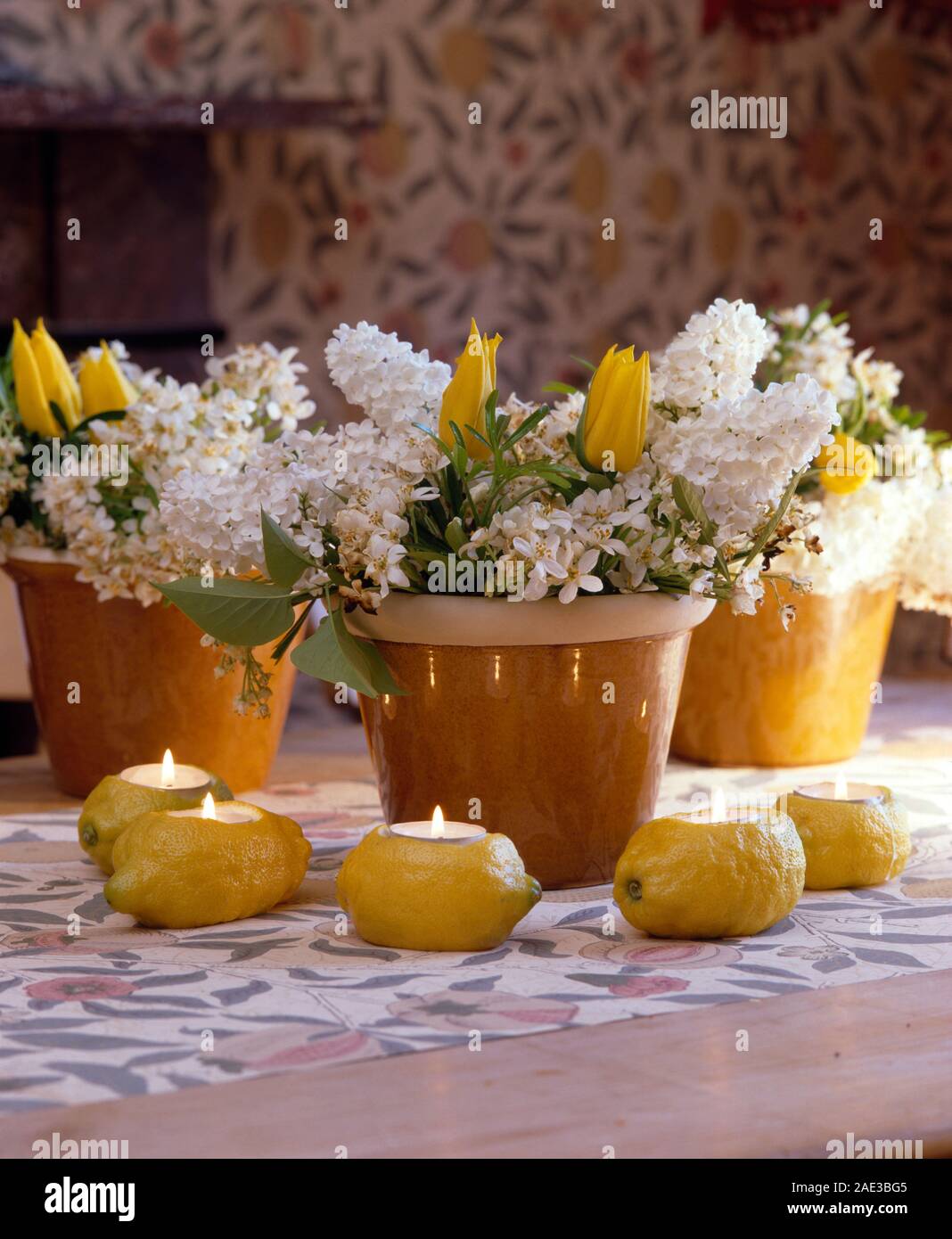 Close-up di raccolto fuori limoni freschi utilizzati come portacandele accanto posies di bianco lilla e tulipani gialli in vasi di colore giallo Foto Stock