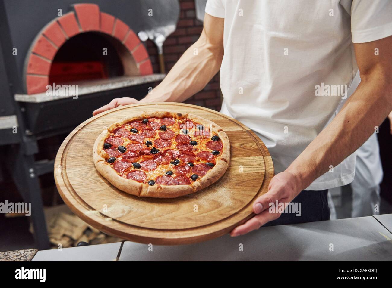 Forti mani dell'uomo. Immagine del preparato una deliziosa pizza con anelli di salsiccia e olive Foto Stock