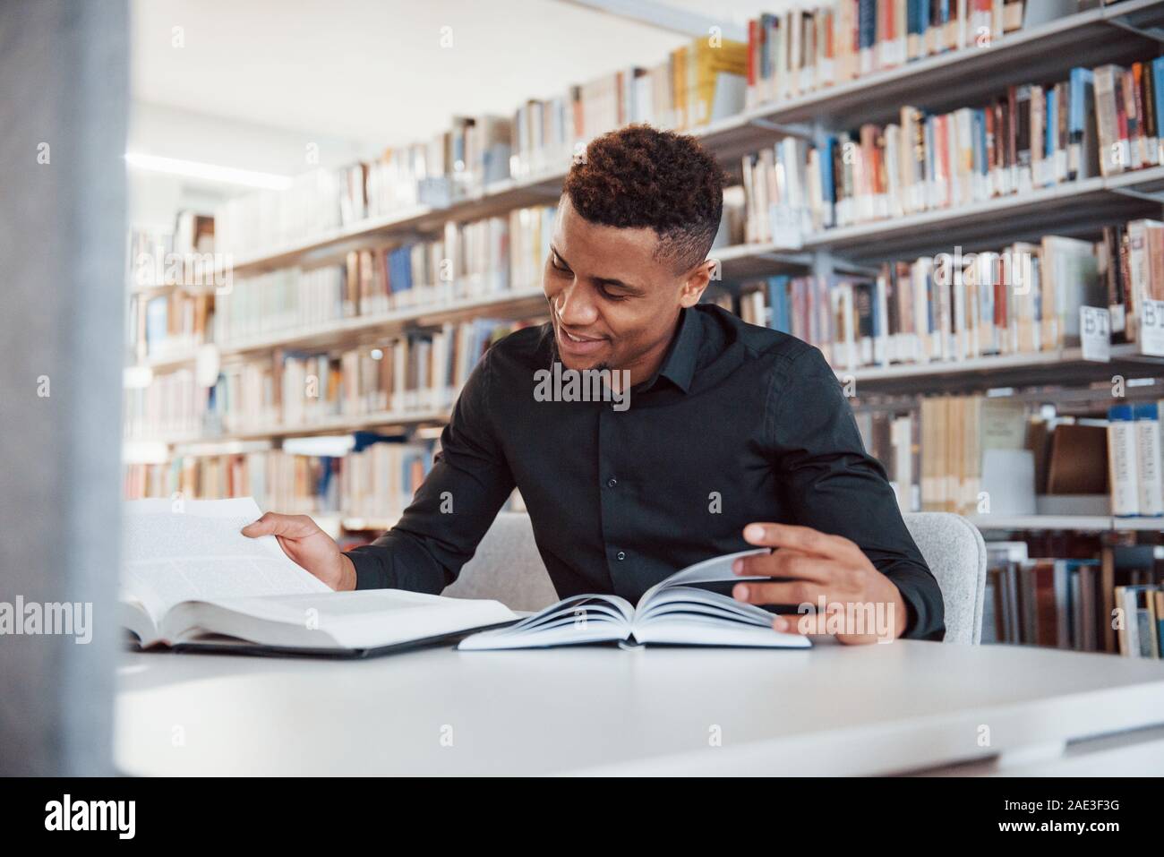 Sorridente durante il processo. African American uomo seduto in biblioteca e la ricerca di alcune informazioni nei libri Foto Stock