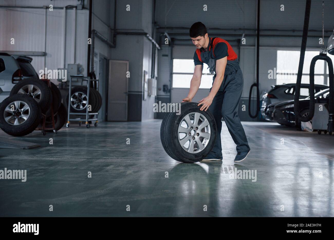 Faremo in modo rapido. Mechanic tenendo un pneumatico in corrispondenza del garage di riparazione. Sostituzione delle gomme invernali ed estive Foto Stock
