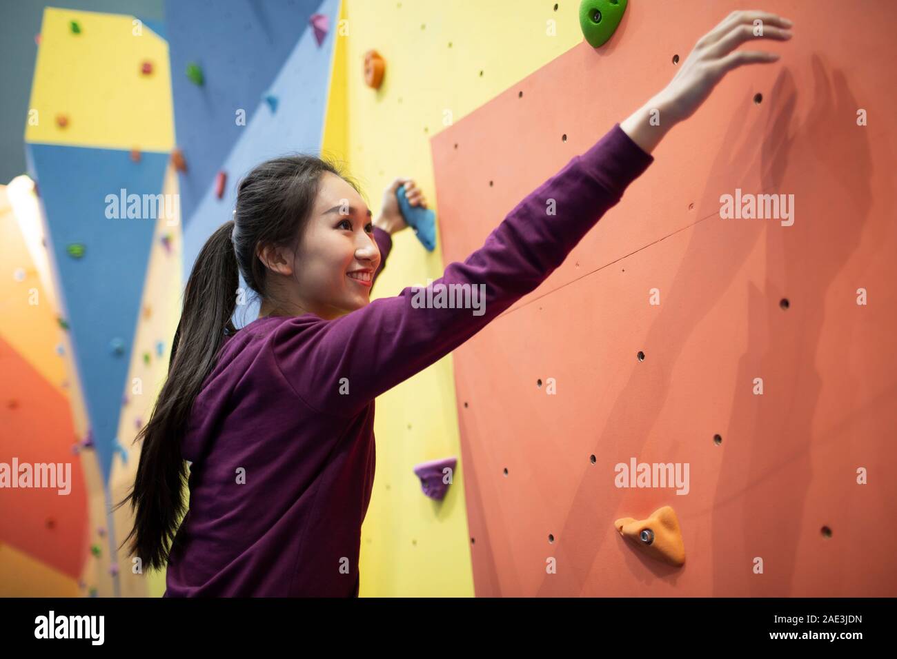 Felice giovane donna scalando una parete di arrampicata in palestra Foto Stock