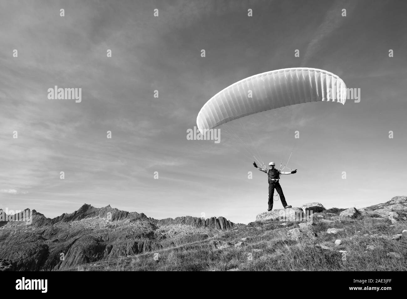 Pilota di parapendio si erge su una roccia e saldi il suo parapendio sopra la sua testa vicino al lago di Grimsel nelle Alpi Svizzere Foto Stock