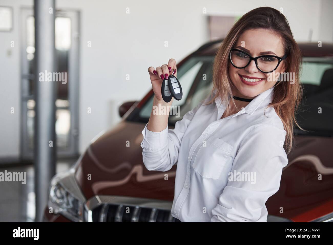 Detiene chiavi in mano. Donna in eyewear e camicia bianca si trova nei pressi dell' automobile rossa Foto Stock